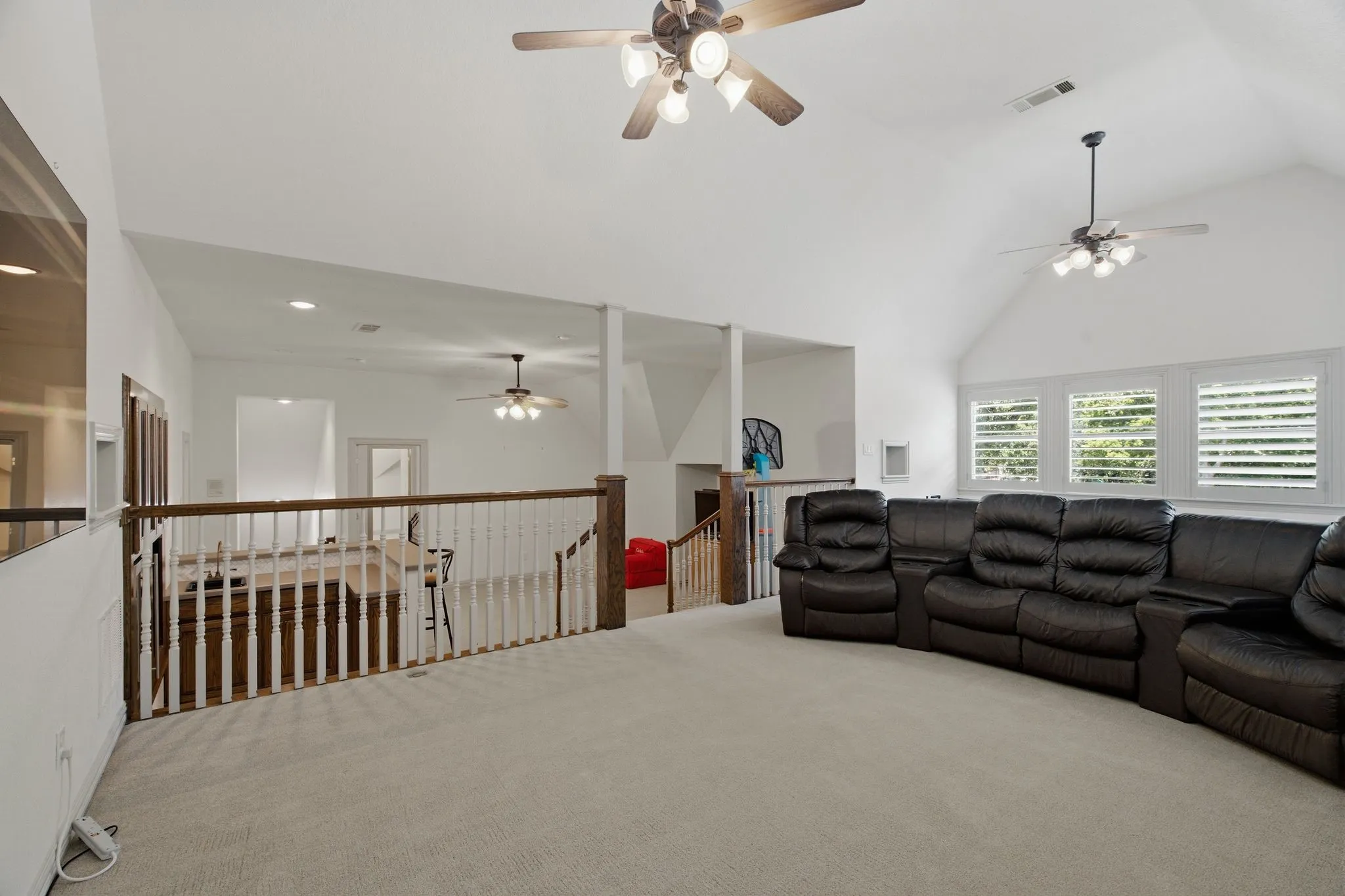 Spacious loft area featuring vaulted ceilings, light-toned carpeting, and a wooden banister overlooking the floor below