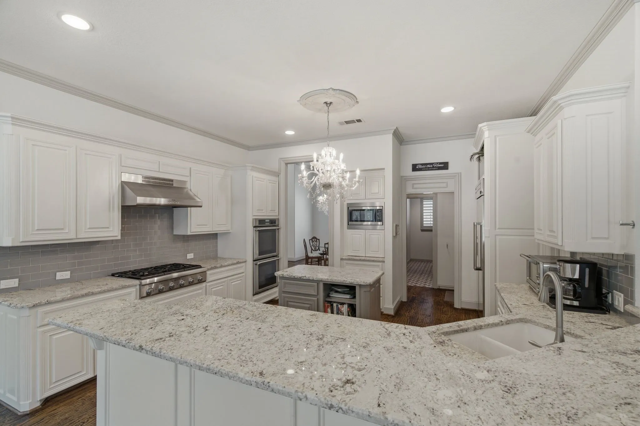Kitchen featuring white shaker-style cabinetry, light speckled countertops, a stainless steel gas range with a matching vent hood, and a built-in double oven