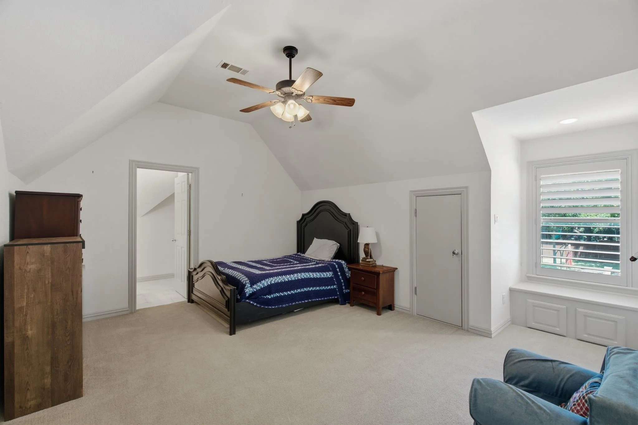 Carpeted room with sloped ceilings and a ceiling fan with light fixture