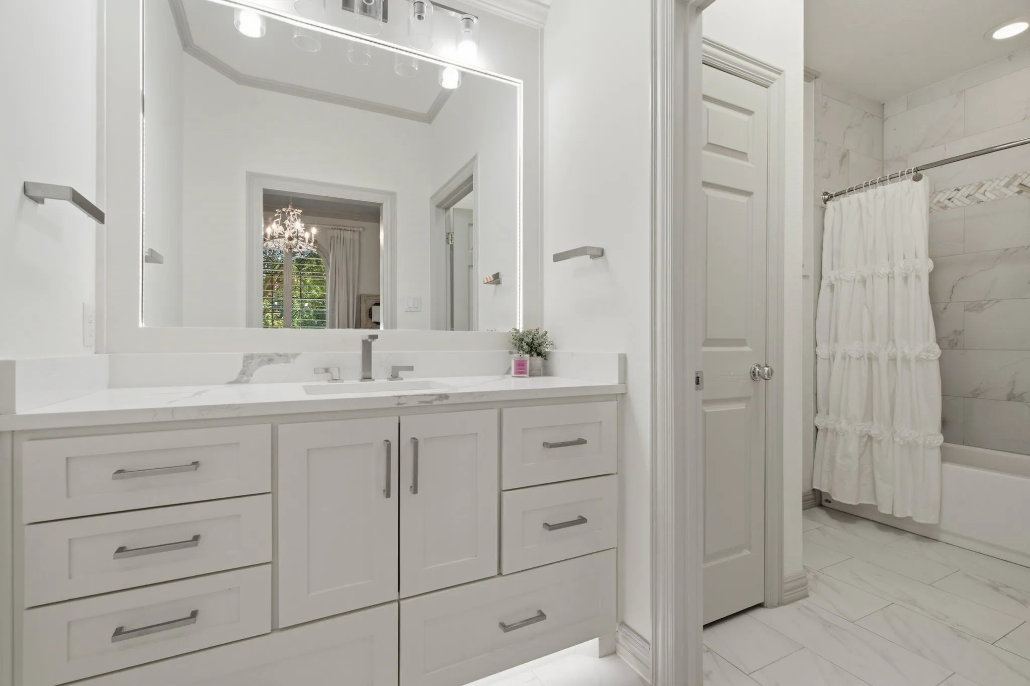 Bathroom featuring a light-toned vanity with dual sinks and ample storage, a large illuminated mirror, and a full bathtub with a shower and tile surround