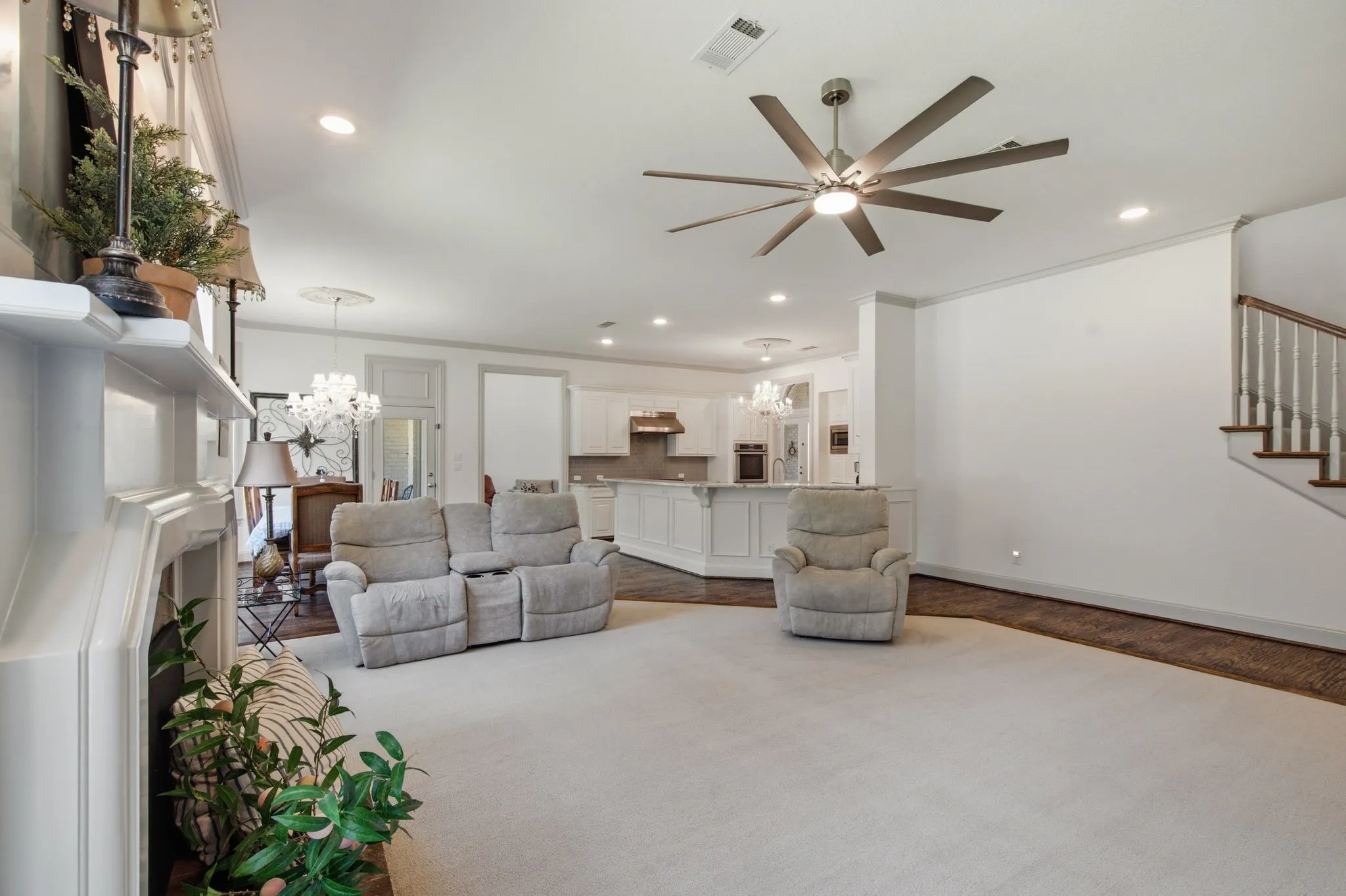 Spacious living area featuring light-colored carpet flooring and a multi-blade ceiling fan with integrated lighting