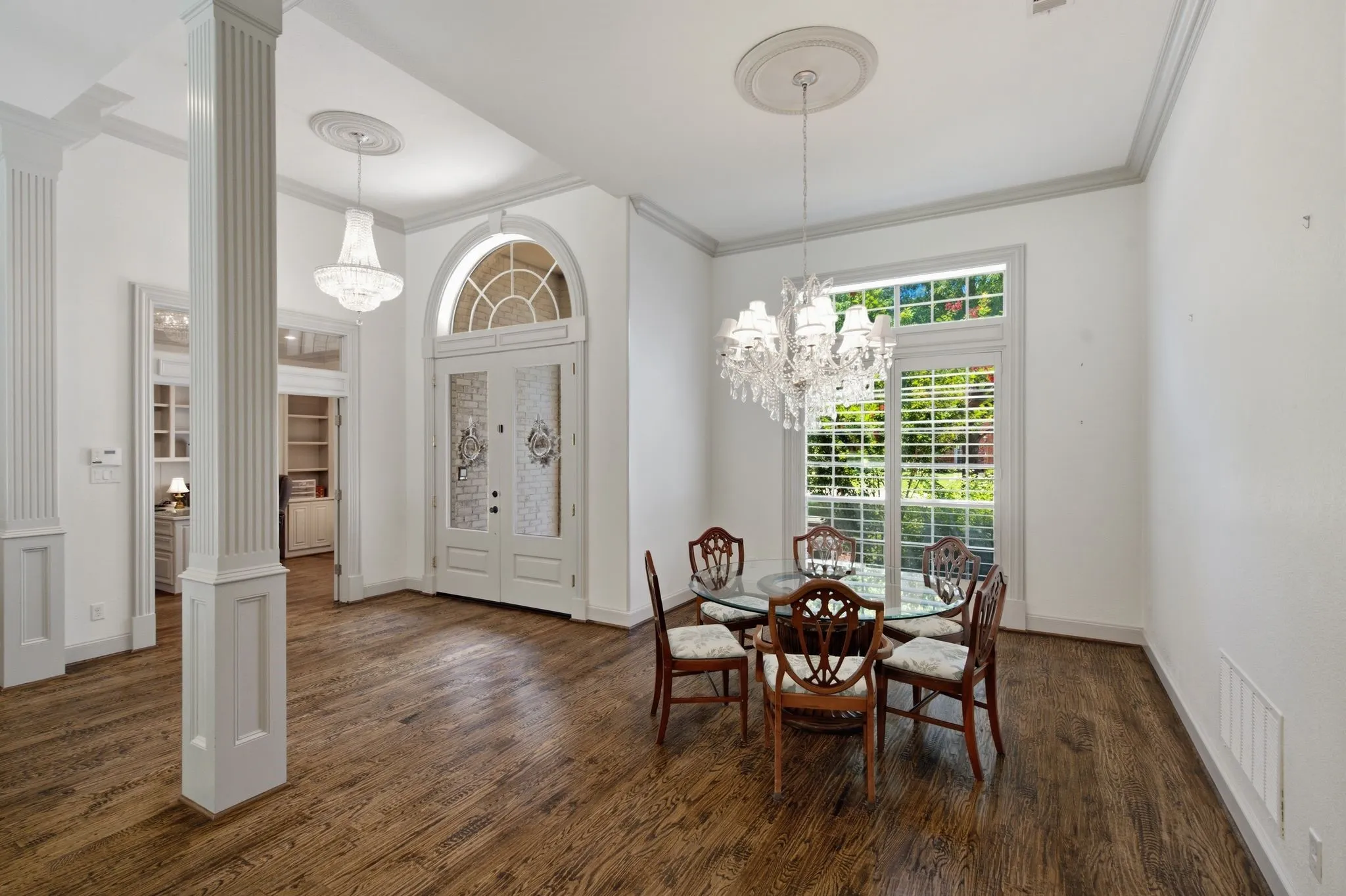 Foyer featuring wood-finish flooring, a crystal chandelier, fluted columns, and a double entry door with an arched transom