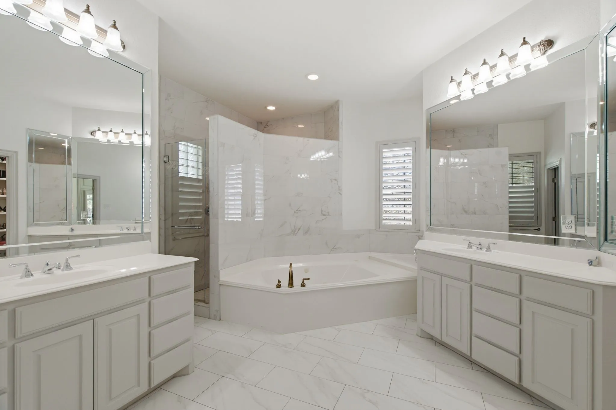 Spacious bathroom featuring dual vanities with integrated sinks, a corner soaking tub, and a separate glass-enclosed shower