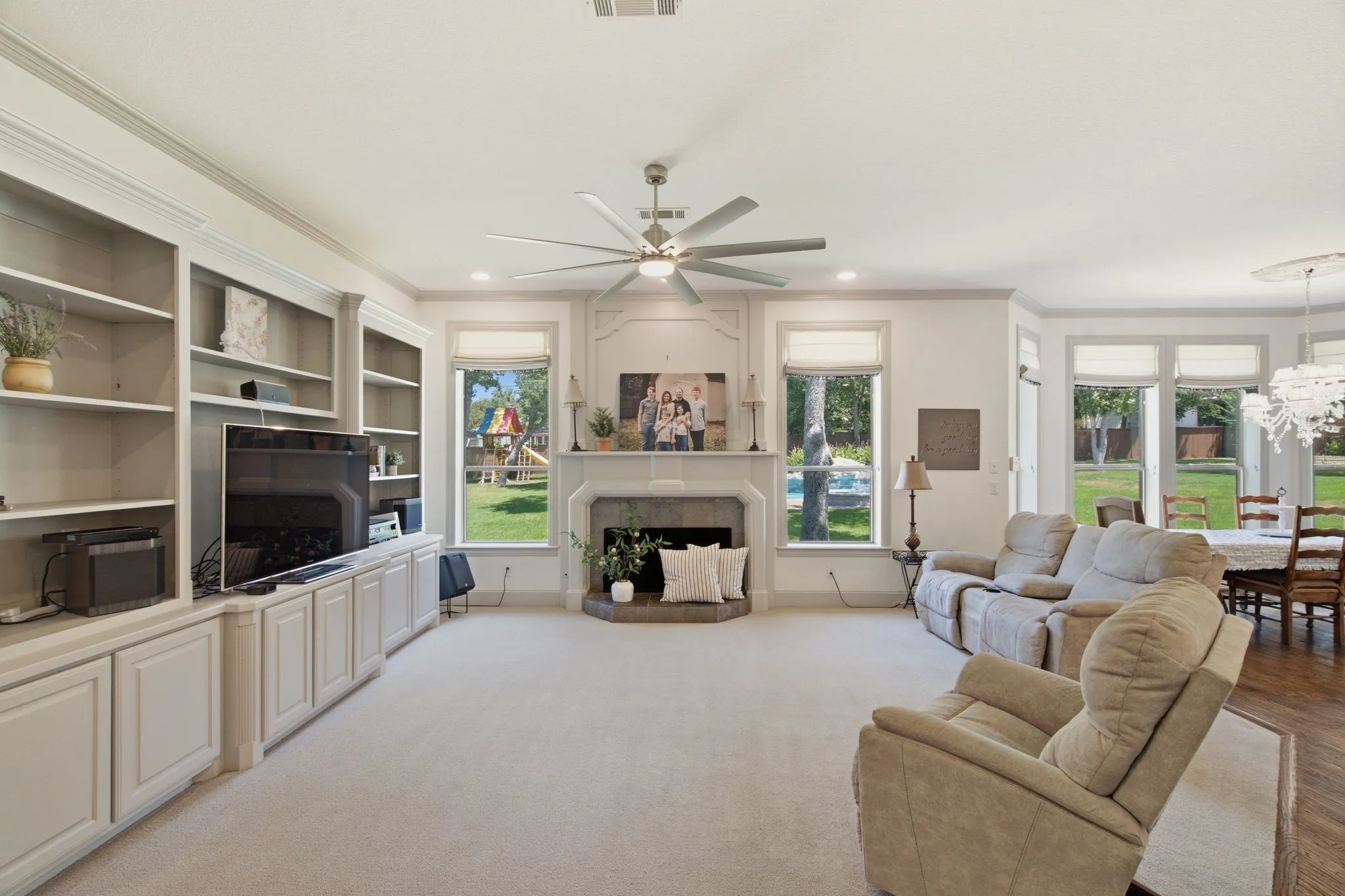 Spacious living area featuring extensive built-in cabinetry, a central fireplace with a stone surround, recessed lighting, and a ceiling fan