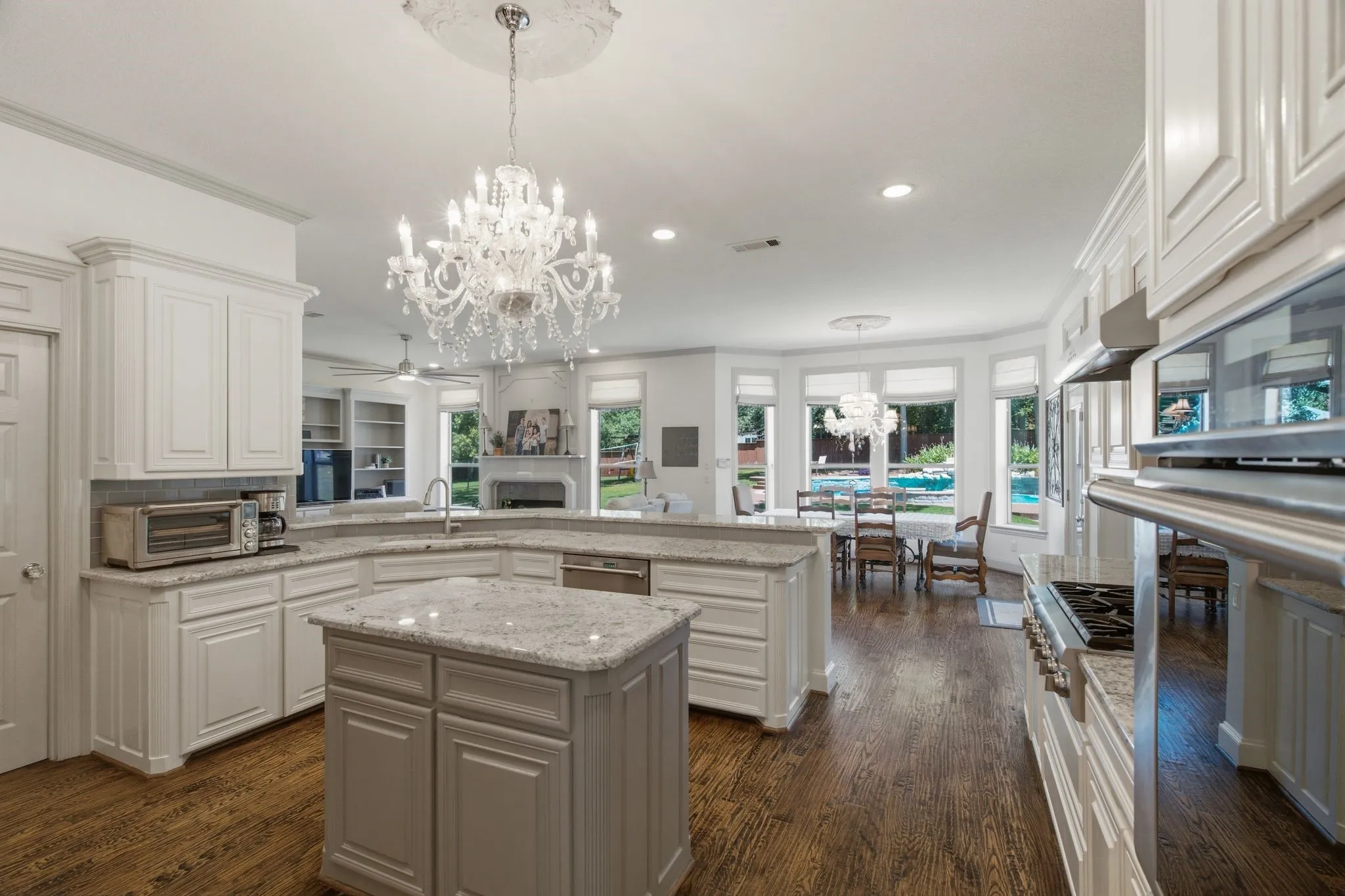 Expansive kitchen featuring a central island with a granite-style countertop, white cabinetry, integrated stainless steel appliances, and wood-finish flooring