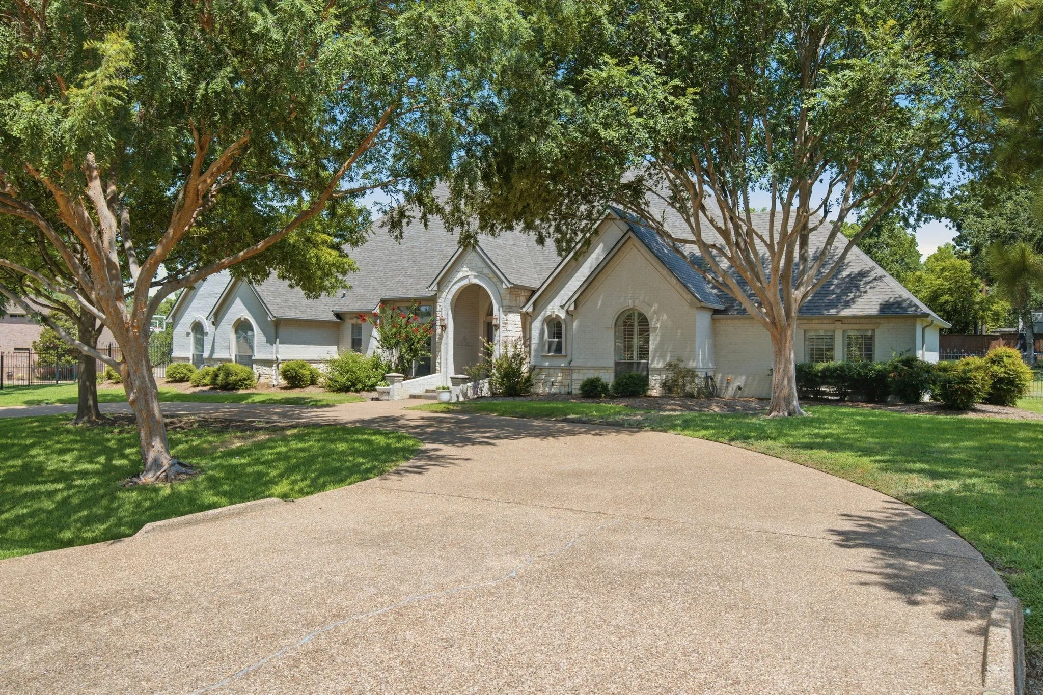 Stucco and stone exterior with a prominent arched entry, surrounded by mature trees