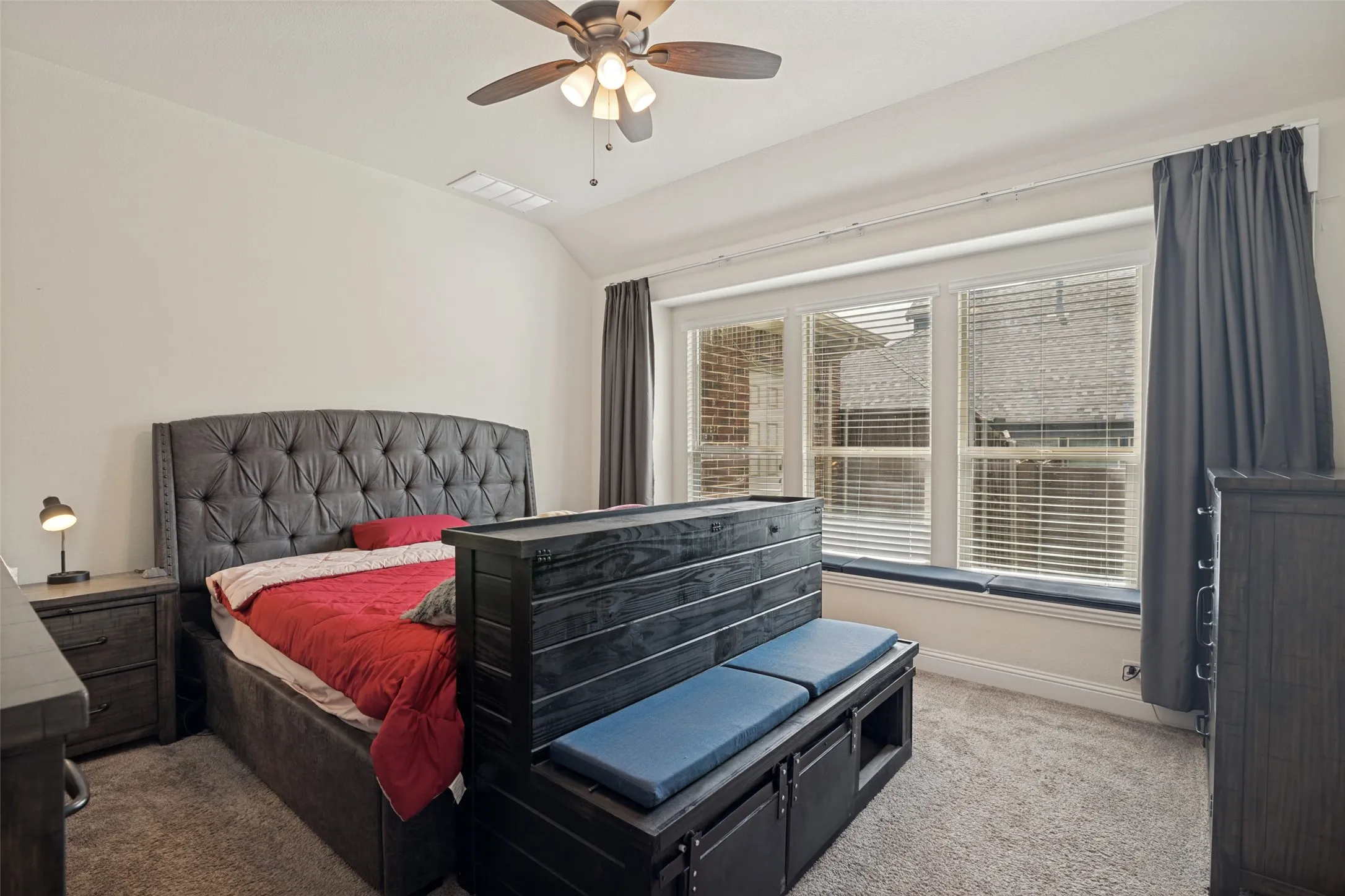 Carpeted room featuring a ceiling fan with light fixture, multiple windows with blinds, and a built-in window seat