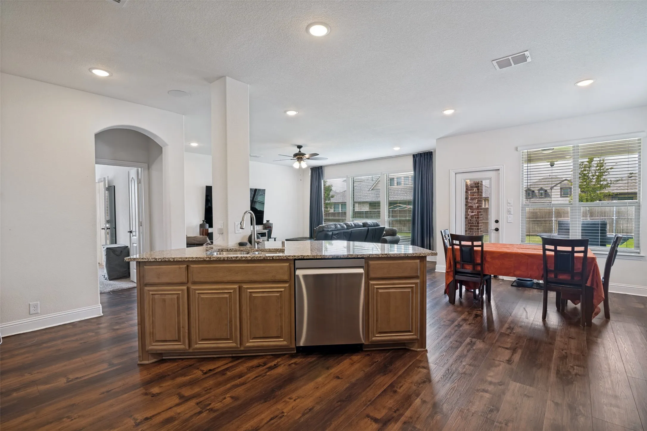 Open-concept kitchen featuring an island with a stainless steel dishwasher, granite-style countertop, and wood cabinetry