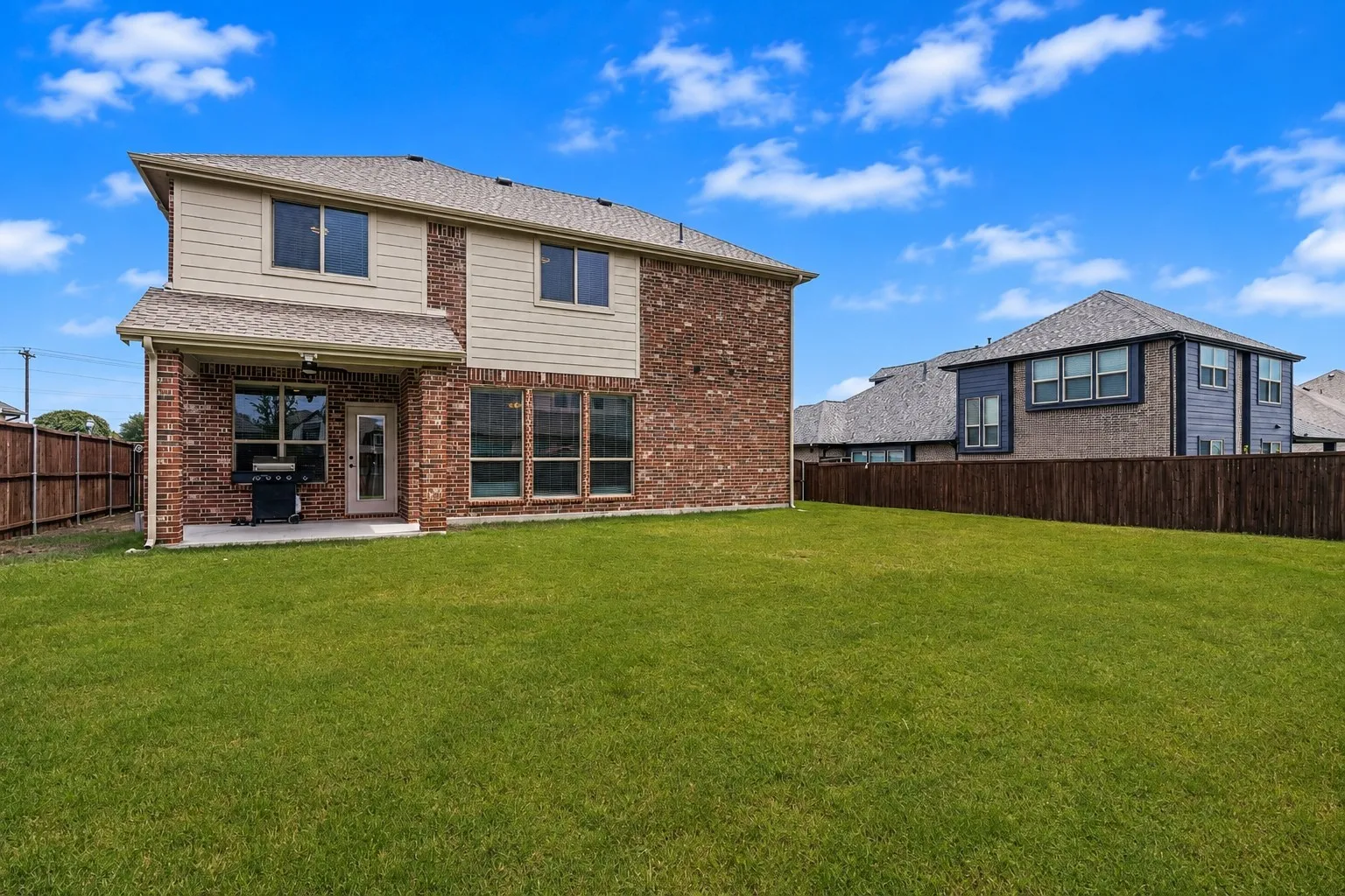 Expansive green lawn with a two-story brick and siding exterior, featuring multiple windows, and a covered patio area