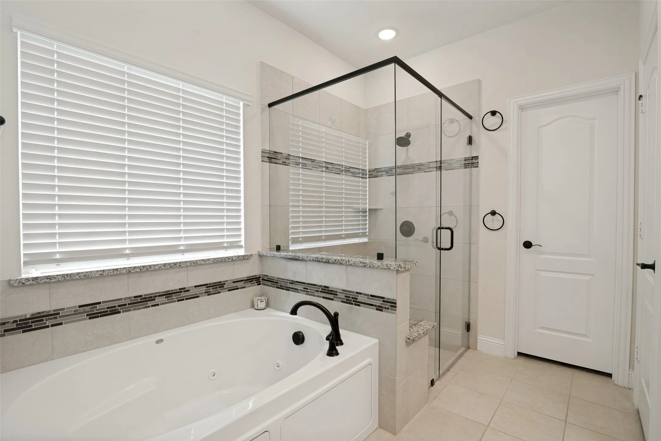 Soaking tub with black fixtures, tiled surround, and integrated window