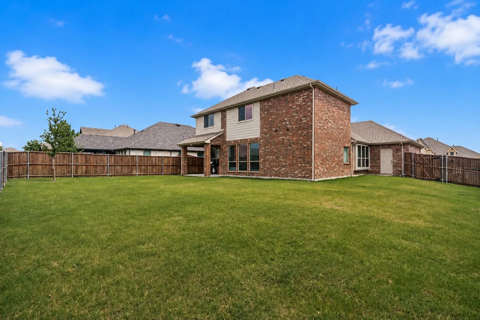 Expansive backyard with a manicured lawn, full privacy fencing, and a covered patio area