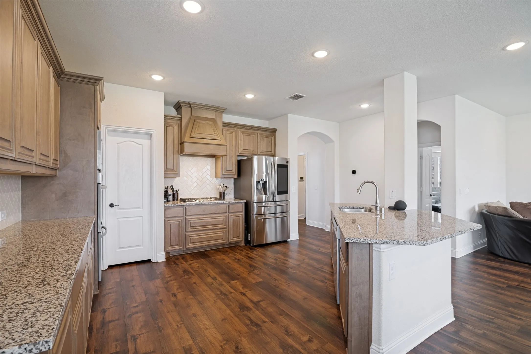 Open-concept kitchen featuring wood-finish flooring, recessed lighting, light-toned cabinetry, granite countertops, and a kitchen island with an undermount sink