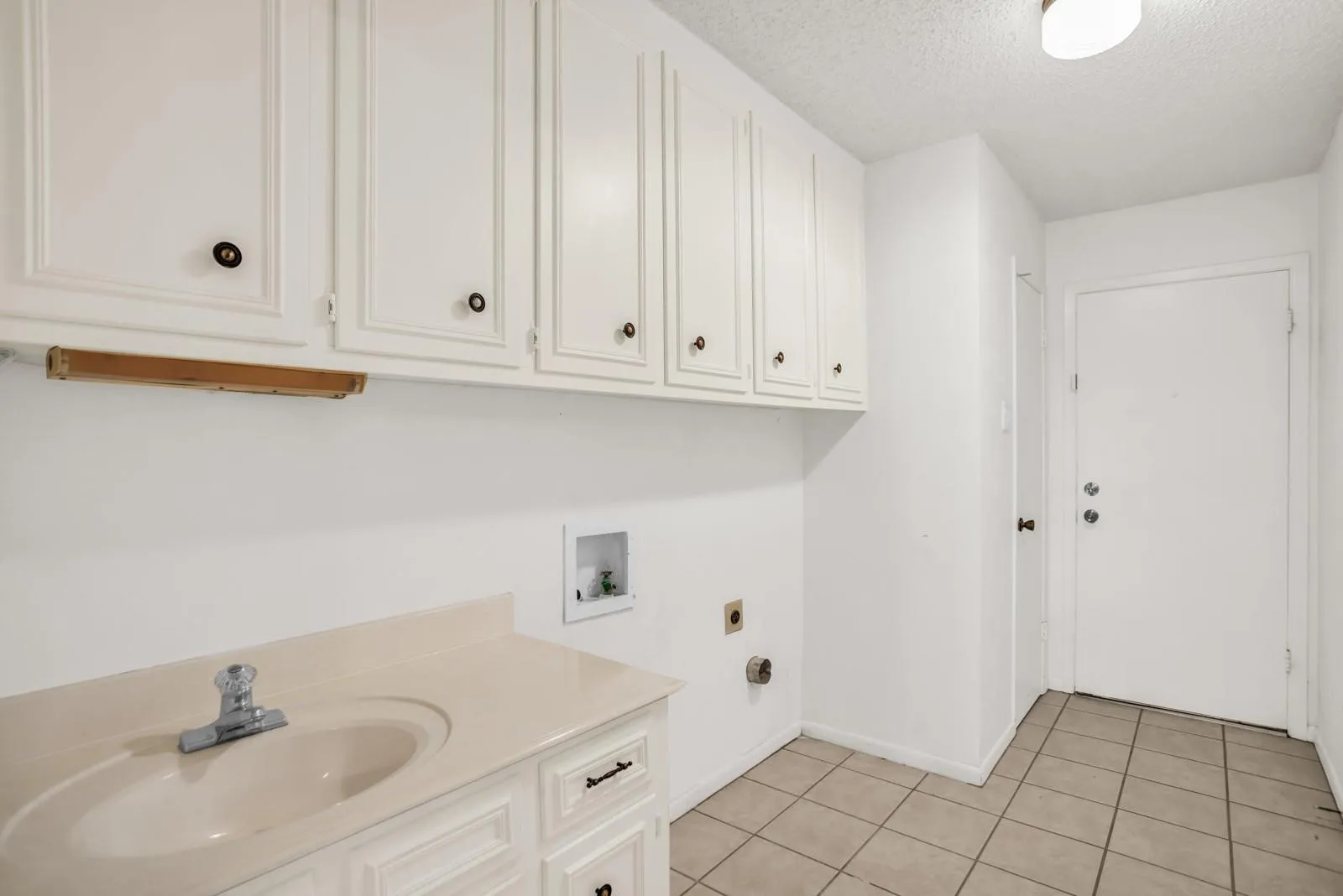 Utility space featuring a single basin vanity with a laminate countertop, overhead white cabinetry, and tiled flooring