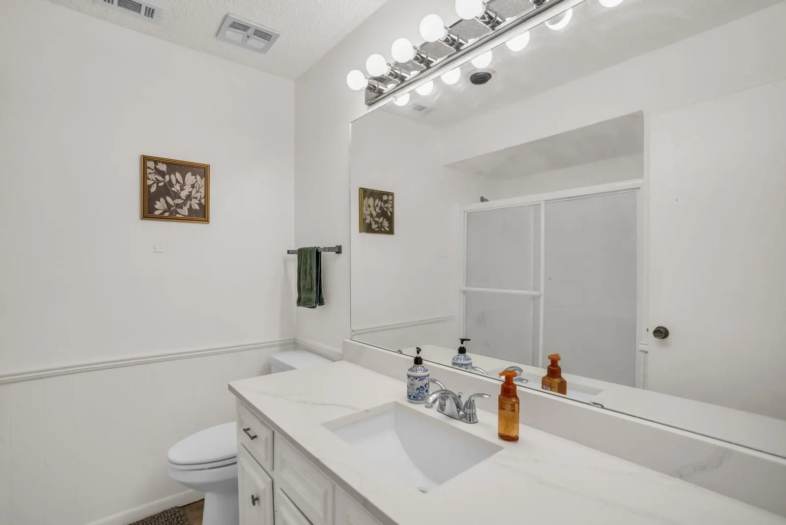 Bathroom vanity featuring a single basin, a chrome faucet, and a large wall-mounted mirror with a vanity light bar
