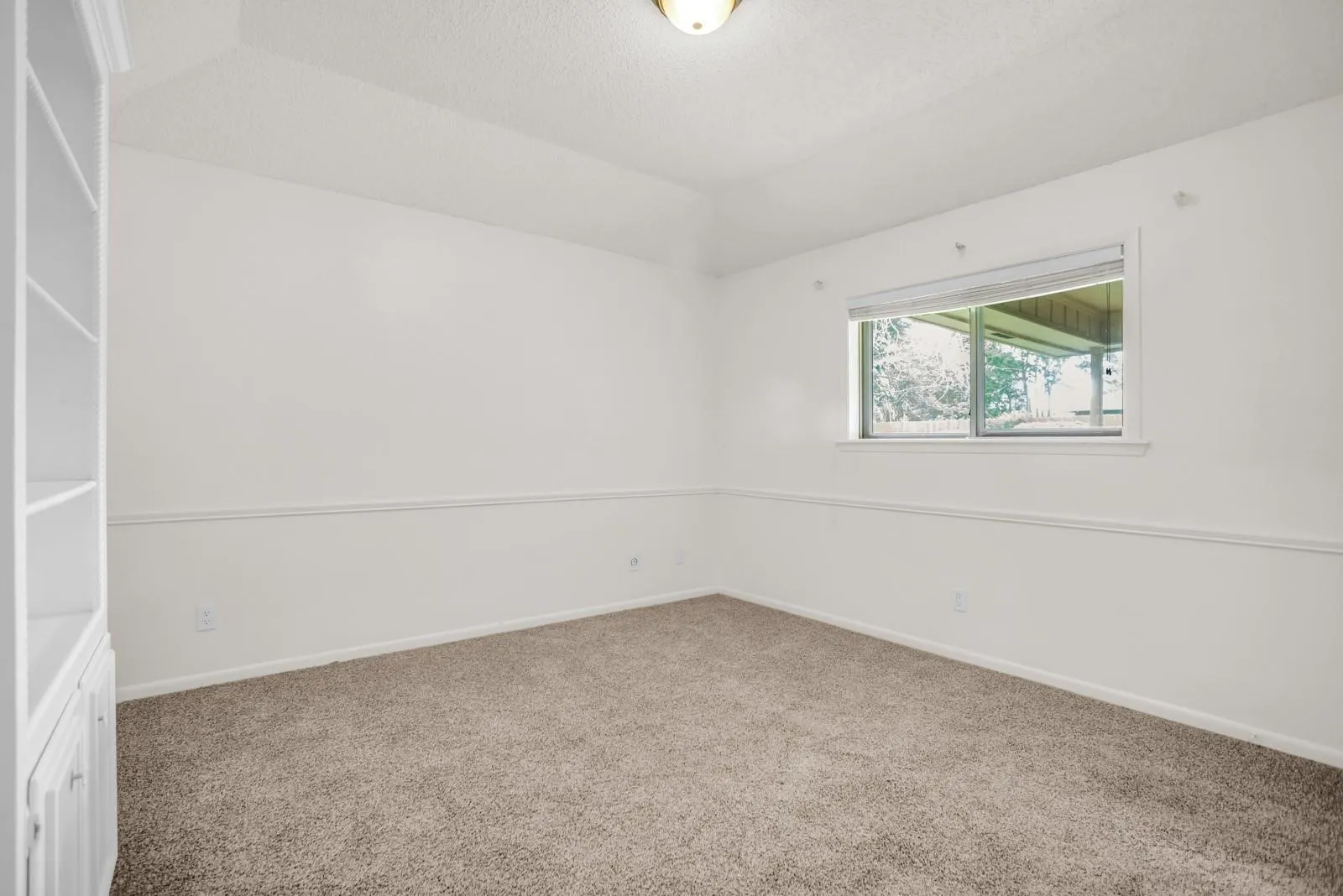 Bright room featuring neutral carpeting, white walls, built-in shelving with lower cabinetry, and a single window