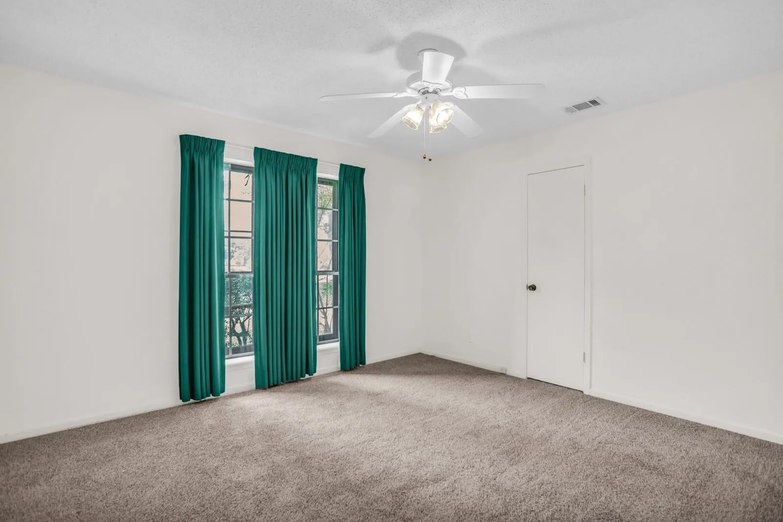 Spacious room featuring gray carpet flooring, white walls, and a ceiling fan with integrated lighting