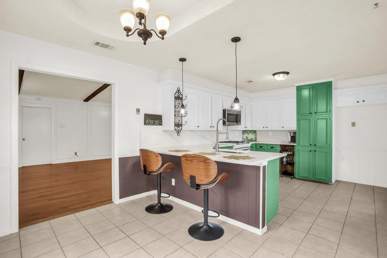 Kitchen featuring white cabinetry, green accent cabinetry, an island with countertop seating, and tile flooring