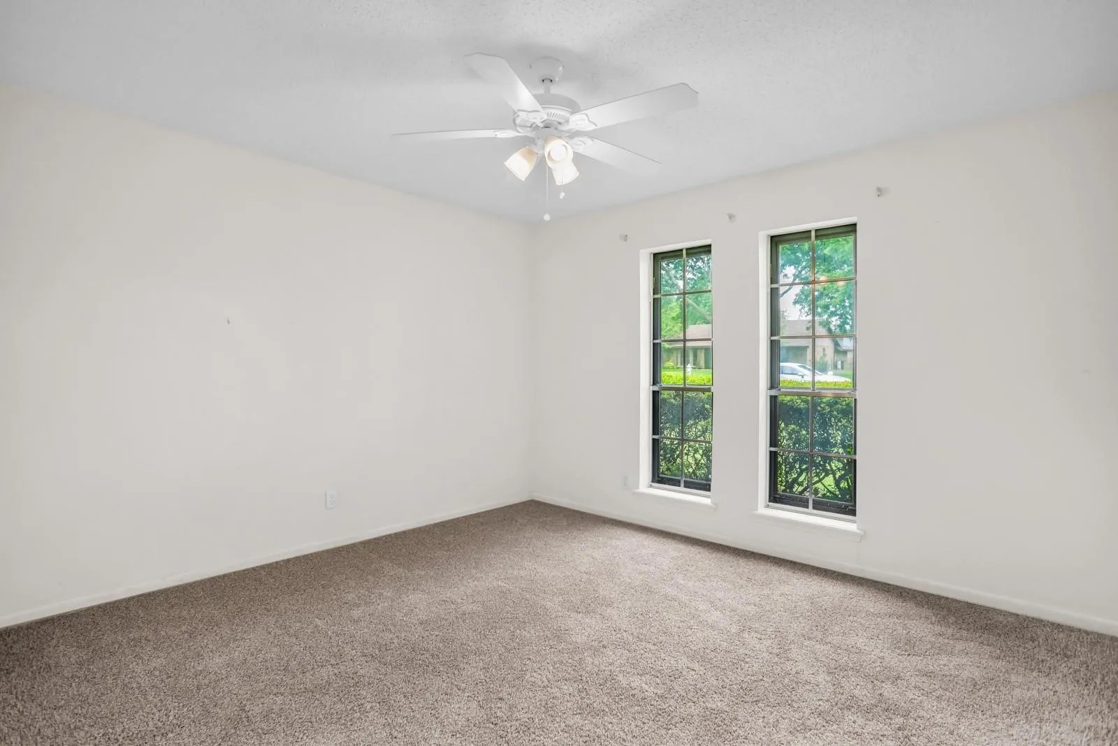 Room featuring two tall windows with dark trim, neutral carpet flooring, a white ceiling fan with light fixture, and white painted walls