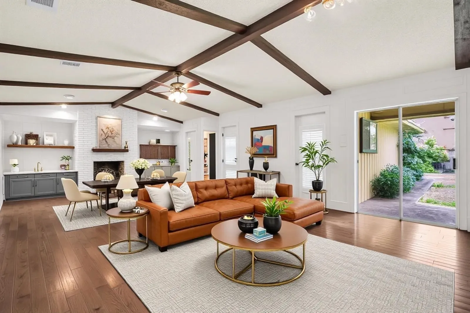 Vaulted ceiling with exposed wood beams, wood-finish flooring, white brick fireplace, built-in wet bar with gray cabinetry, and sliding glass patio doors