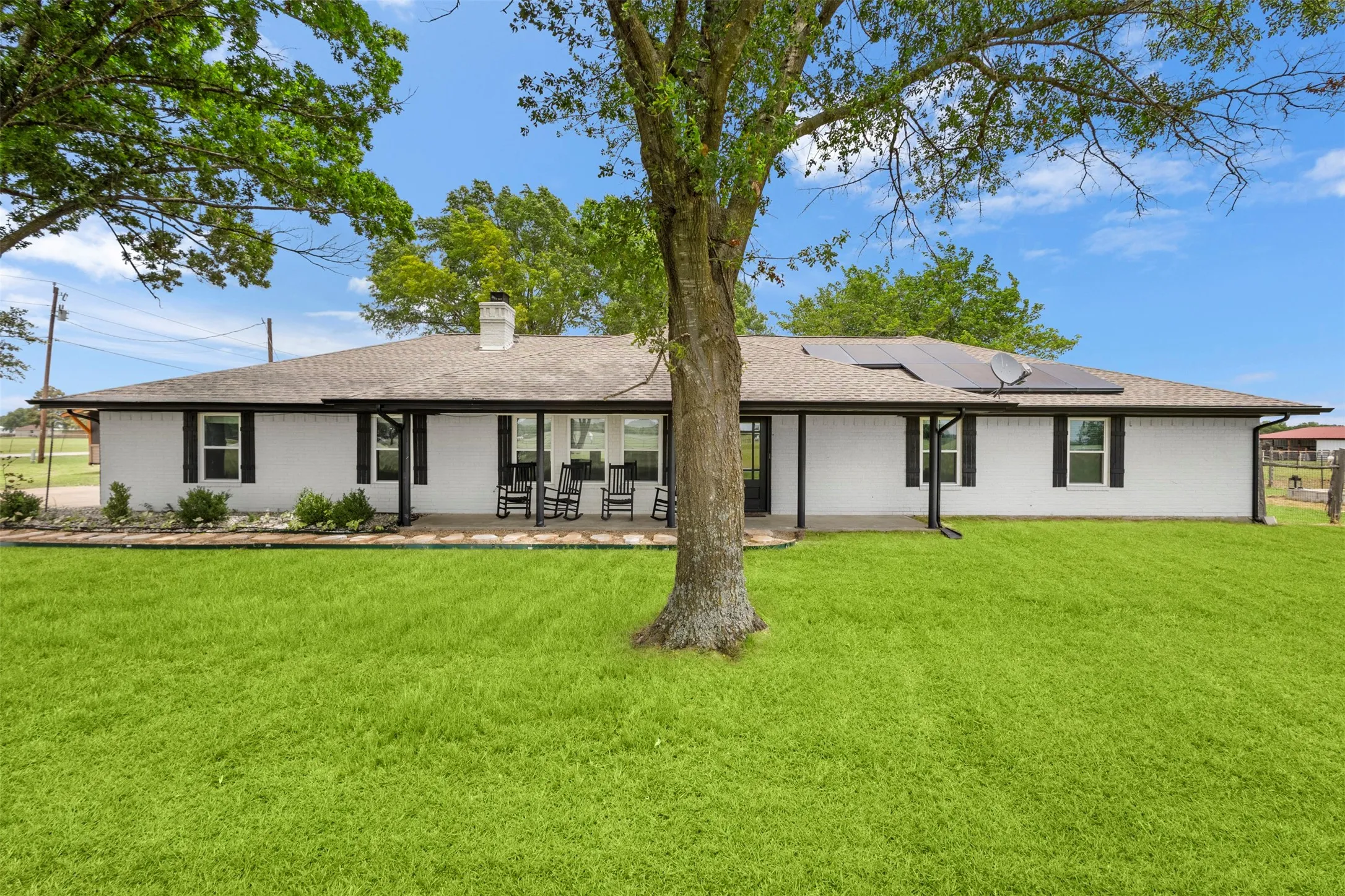 Expansive green lawn surrounds a white-painted brick exterior with black shutters and a covered patio