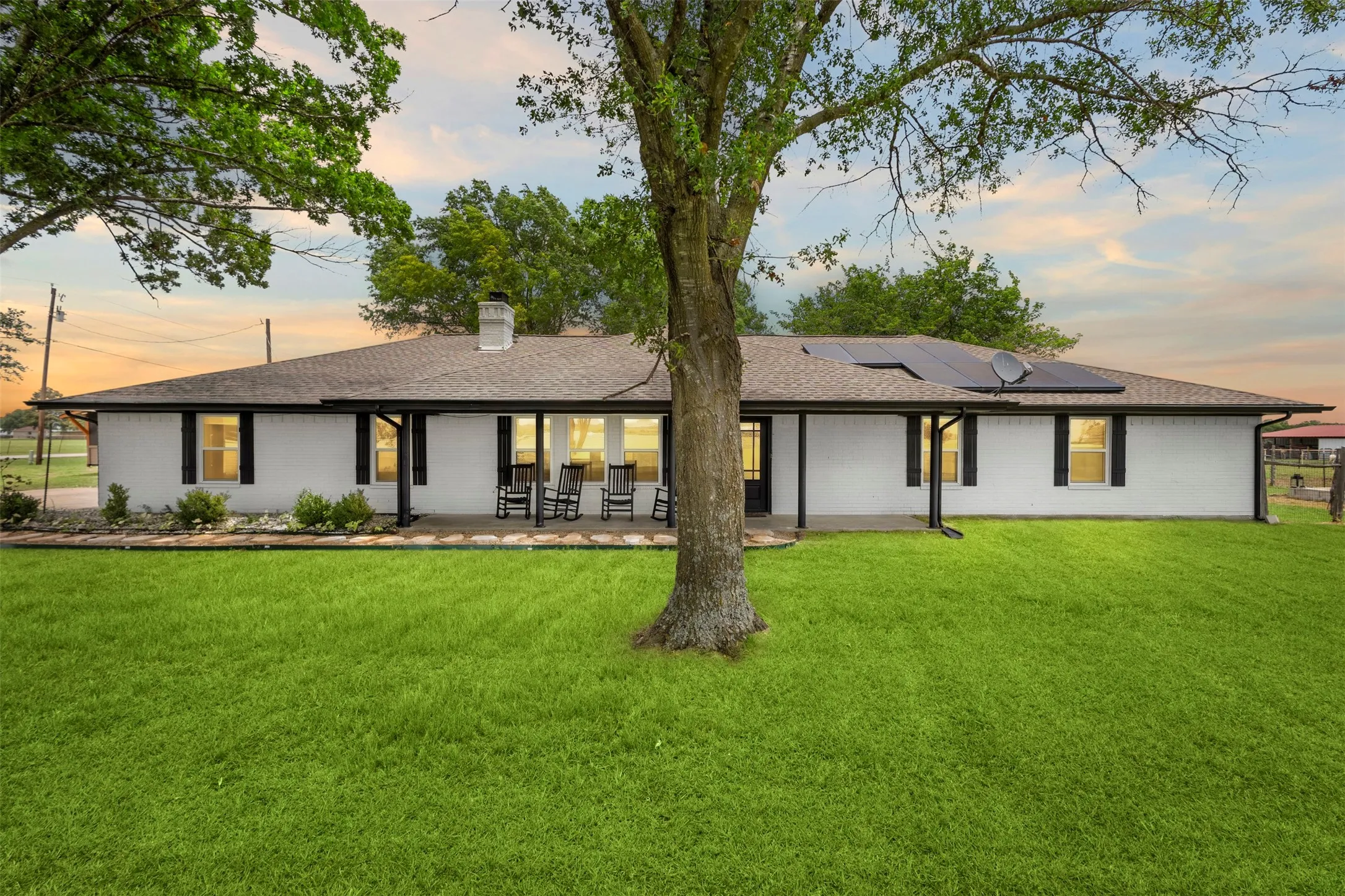 Ranch-style exterior with white siding, a dark roof, and black window shutters