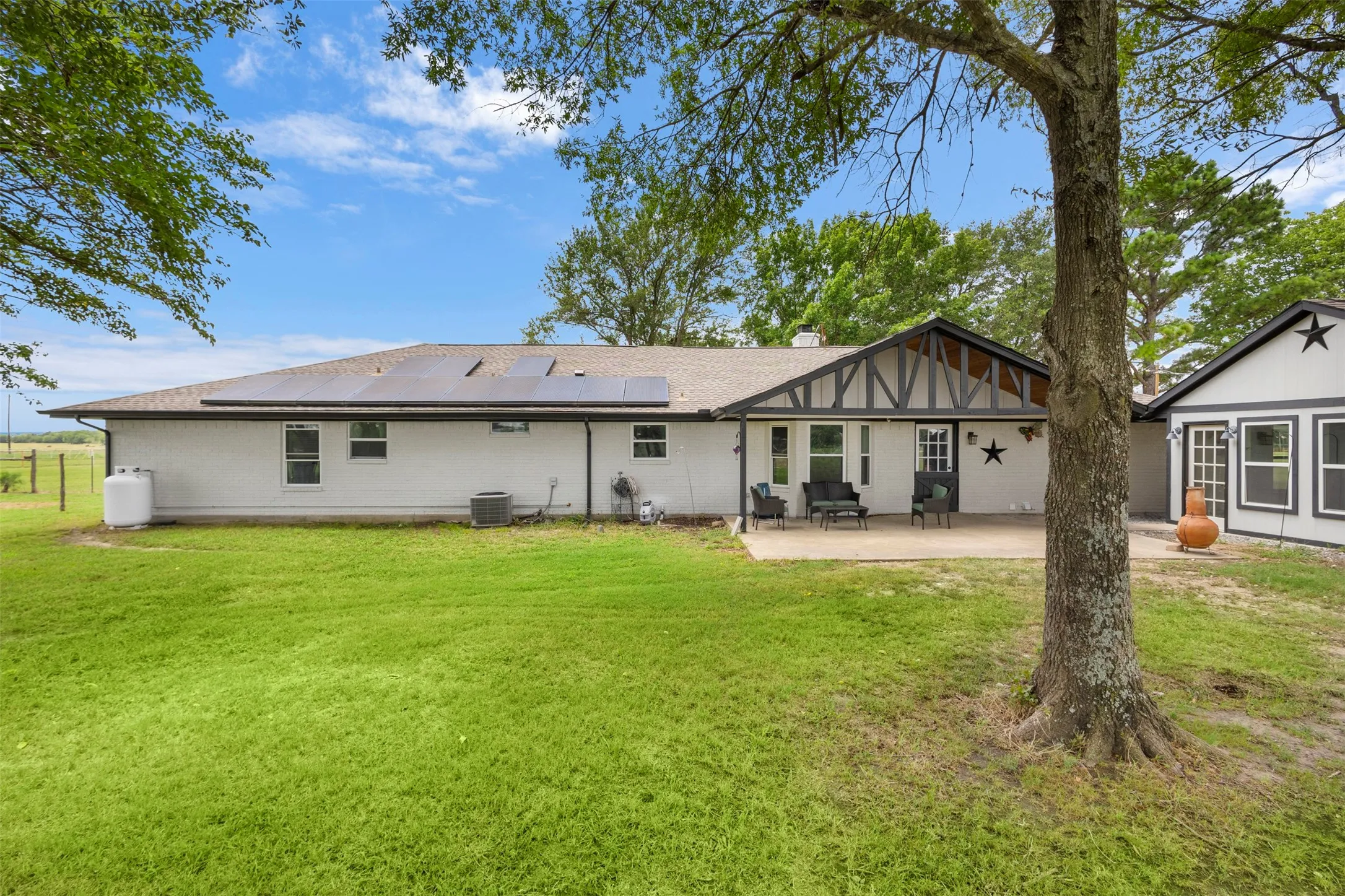 Spacious rear yard with a paved patio, white exterior siding, and a gabled roofline featuring solar panels