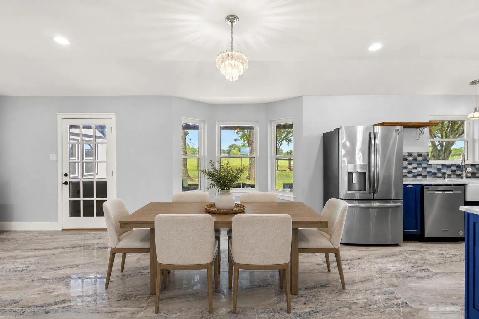 Bay window offering ample natural light, recessed ceiling lighting, elegant crystal chandelier, glass-paneled exterior door, and stainless steel kitchen appliances