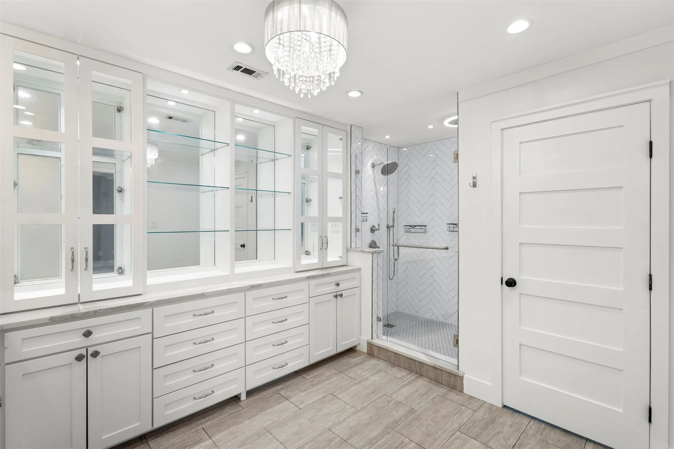 Spacious bathroom with extensive built-in white cabinetry, glass shelving, and light-toned countertops