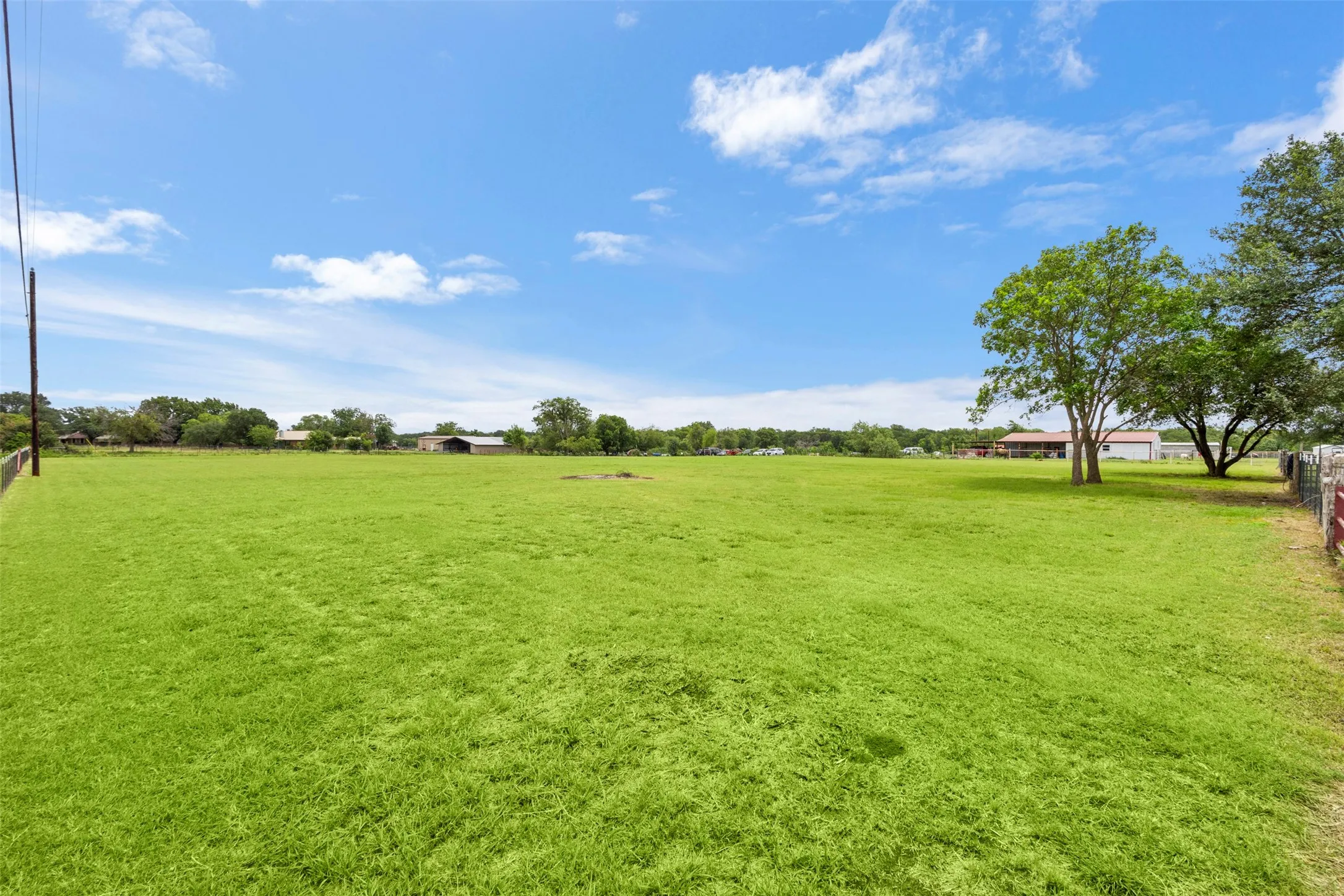 Expansive green field featuring distant structures and mature trees
