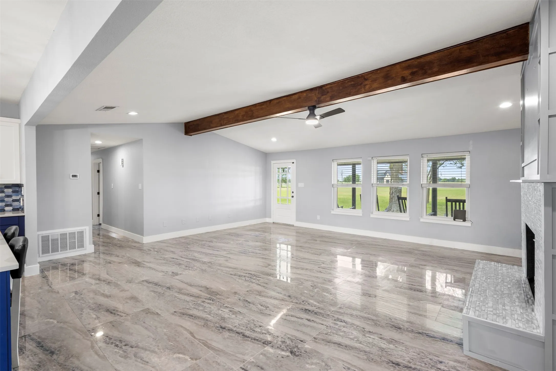 Spacious living area featuring high vaulted ceilings with a prominent wood beam, large format tile flooring, and recessed lighting