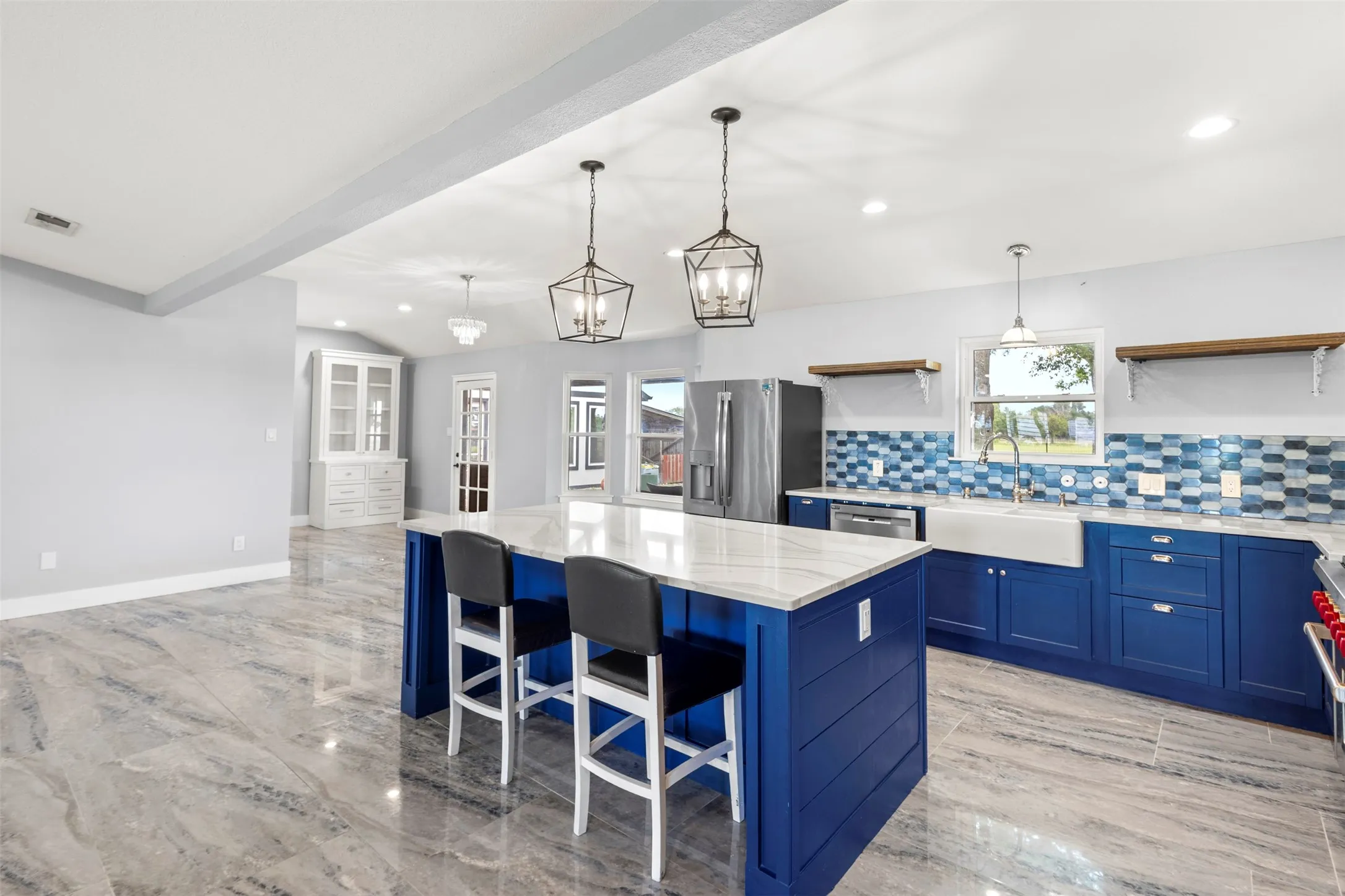 Spacious kitchen featuring a large central island with a white countertop, vibrant blue cabinetry, and a multi-tone blue tile backsplash