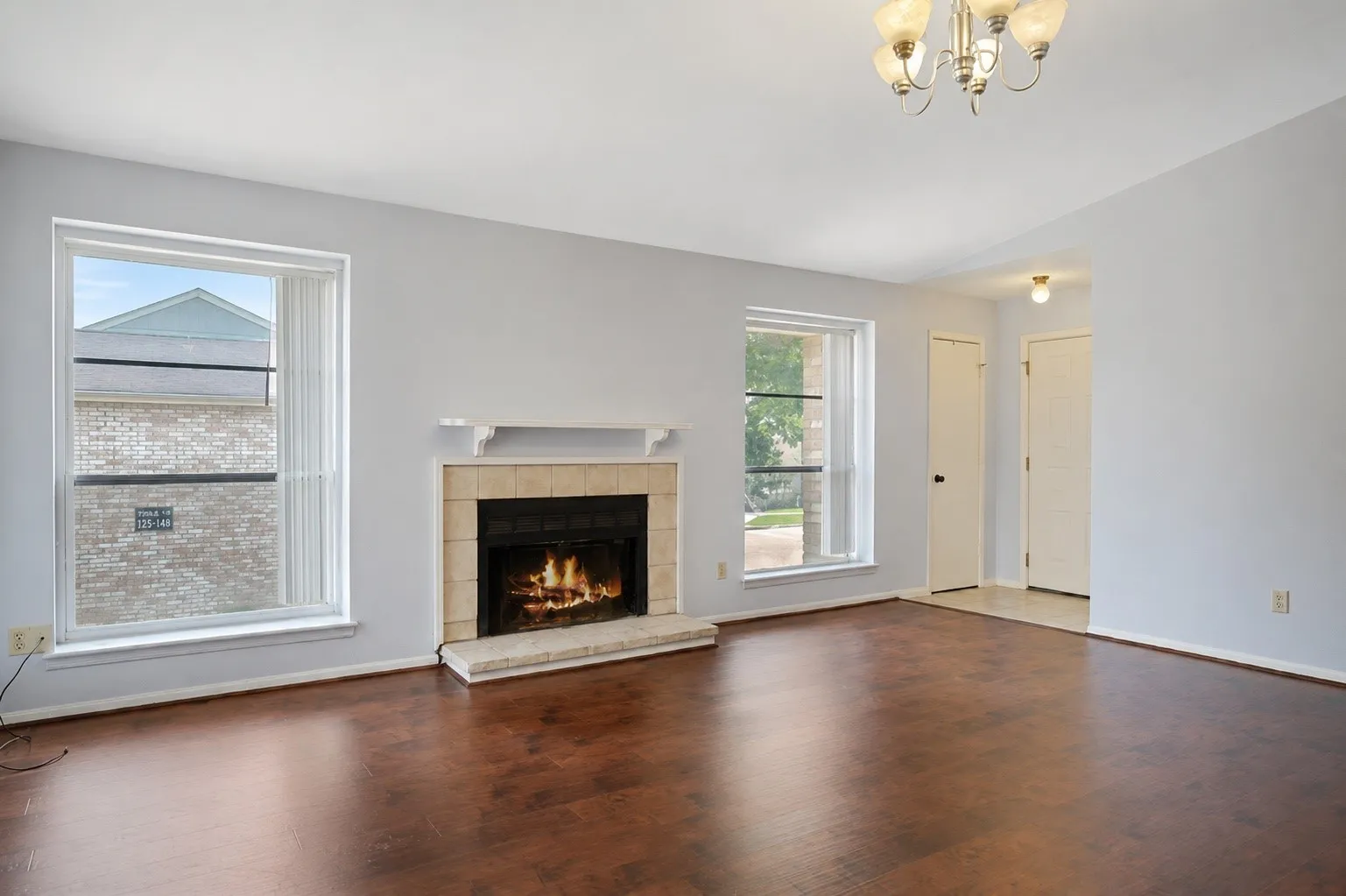 Living area featuring wood-finish flooring, a tiled fireplace with a mantel, and two large windows
