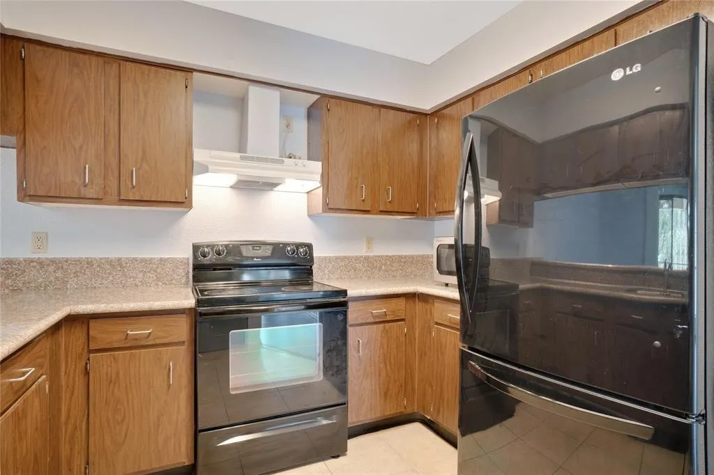 Kitchen featuring wood-finish cabinetry, speckled countertops, black electric range with overhead ventilation, and a black refrigerator