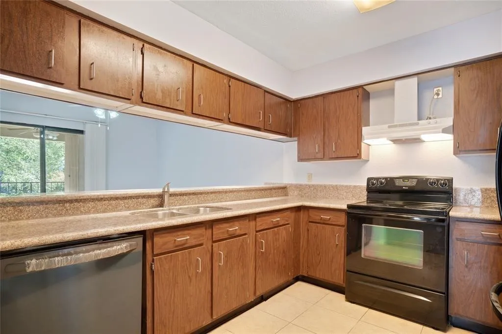 Kitchen featuring wood cabinetry, stone-look countertops, a double basin sink, black range, and black dishwasher