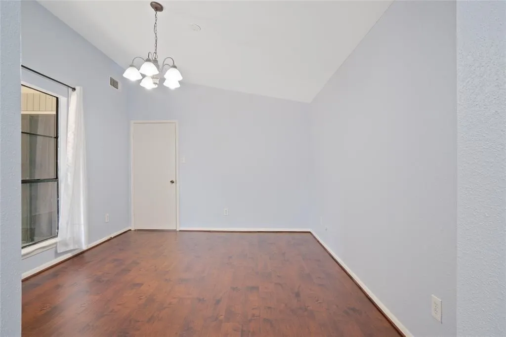 Spacious room featuring wood-finish flooring, light blue wall paint, a vaulted ceiling, and a multi-light chandelier