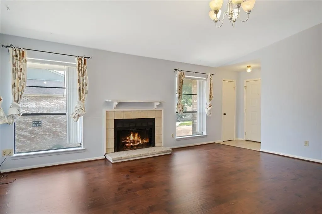 Living area featuring wood-finish flooring, a tile-surround fireplace with a white mantel, and multiple windows