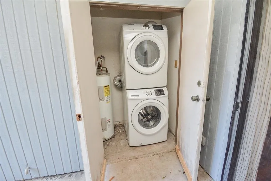 Utility closet featuring a stacked washer and dryer unit, a water heater, and light-colored louvered door
