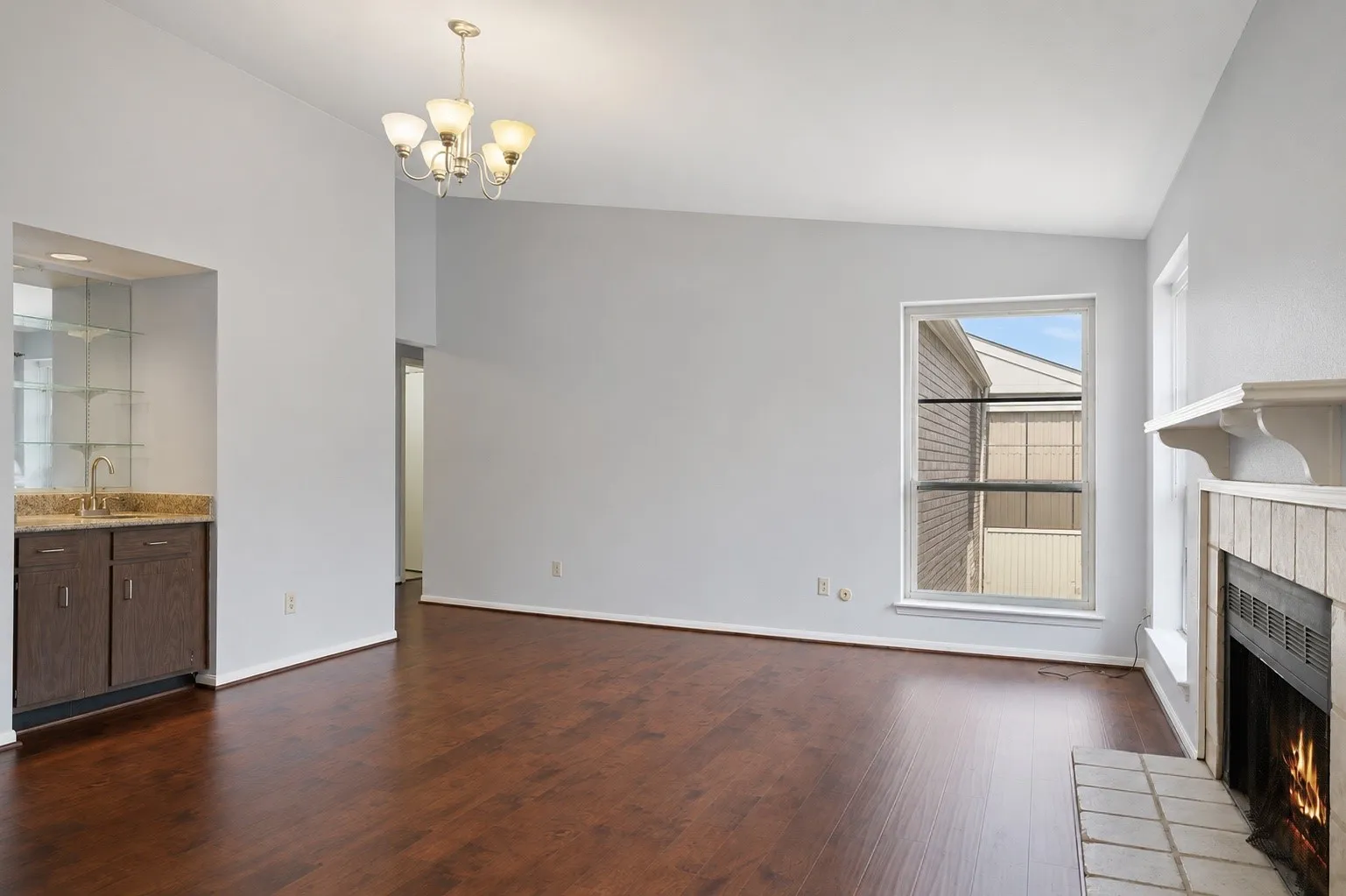 Open living area featuring wood-finish flooring, a built-in wet bar with a granite-style countertop, and a fireplace with a tiled hearth and mantle