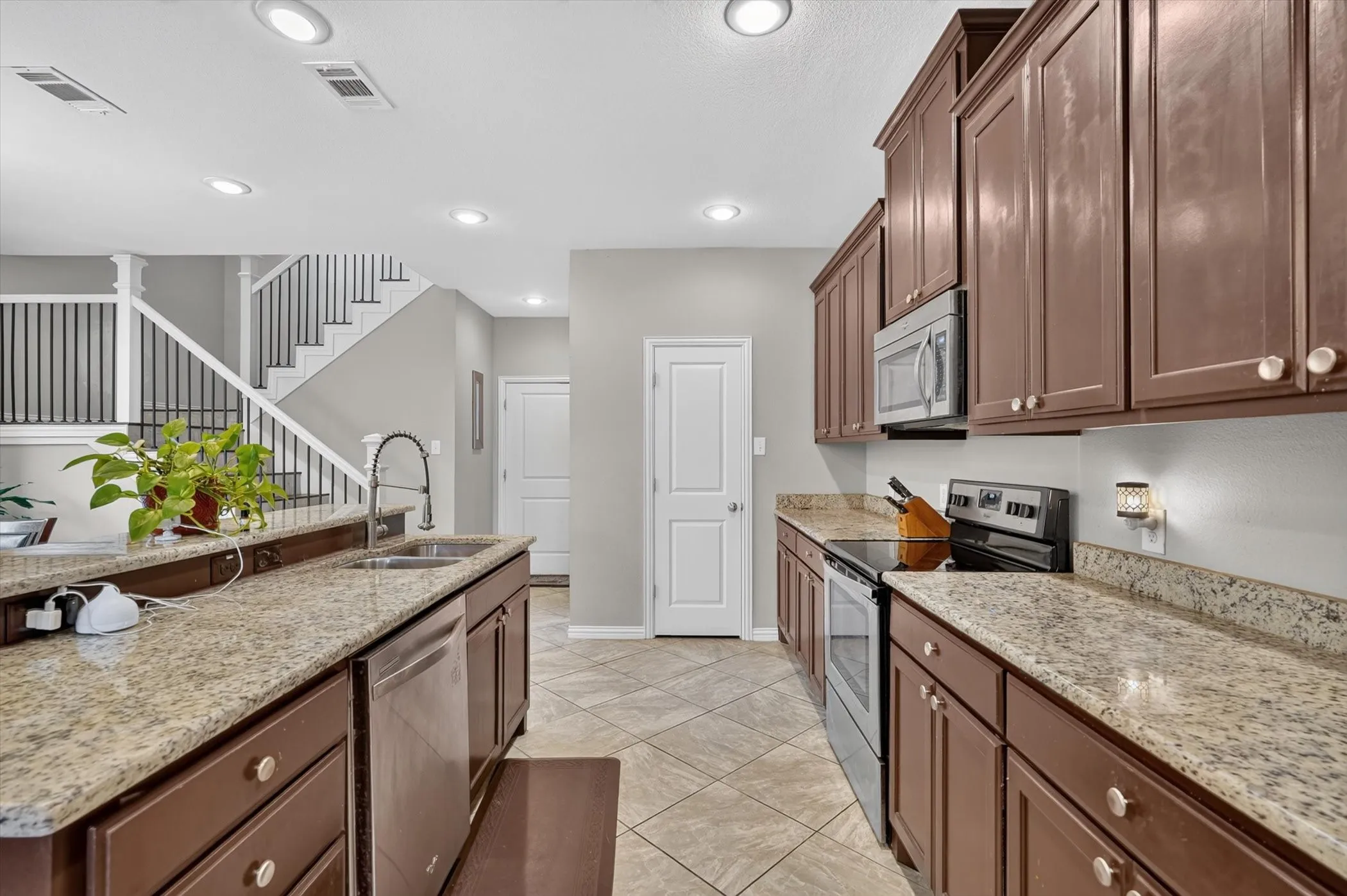 Kitchen featuring granite countertops, wood-finish cabinetry, stainless steel appliances, and diagonal tile flooring