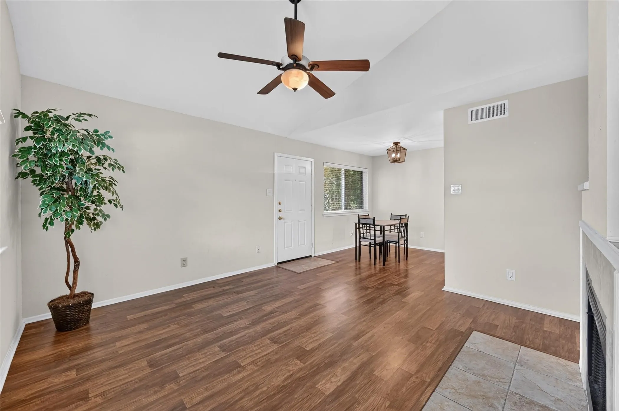 Spacious living area featuring wood-finish flooring, a vaulted ceiling, and a ceiling fan with integrated lighting