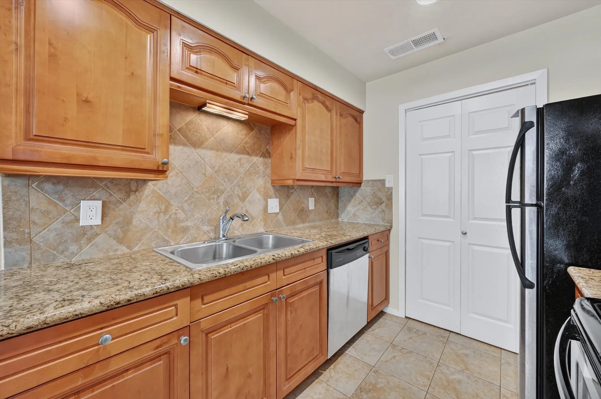 Kitchen featuring wood cabinetry, granite-style countertops, a stainless steel double sink, and a tile backsplash