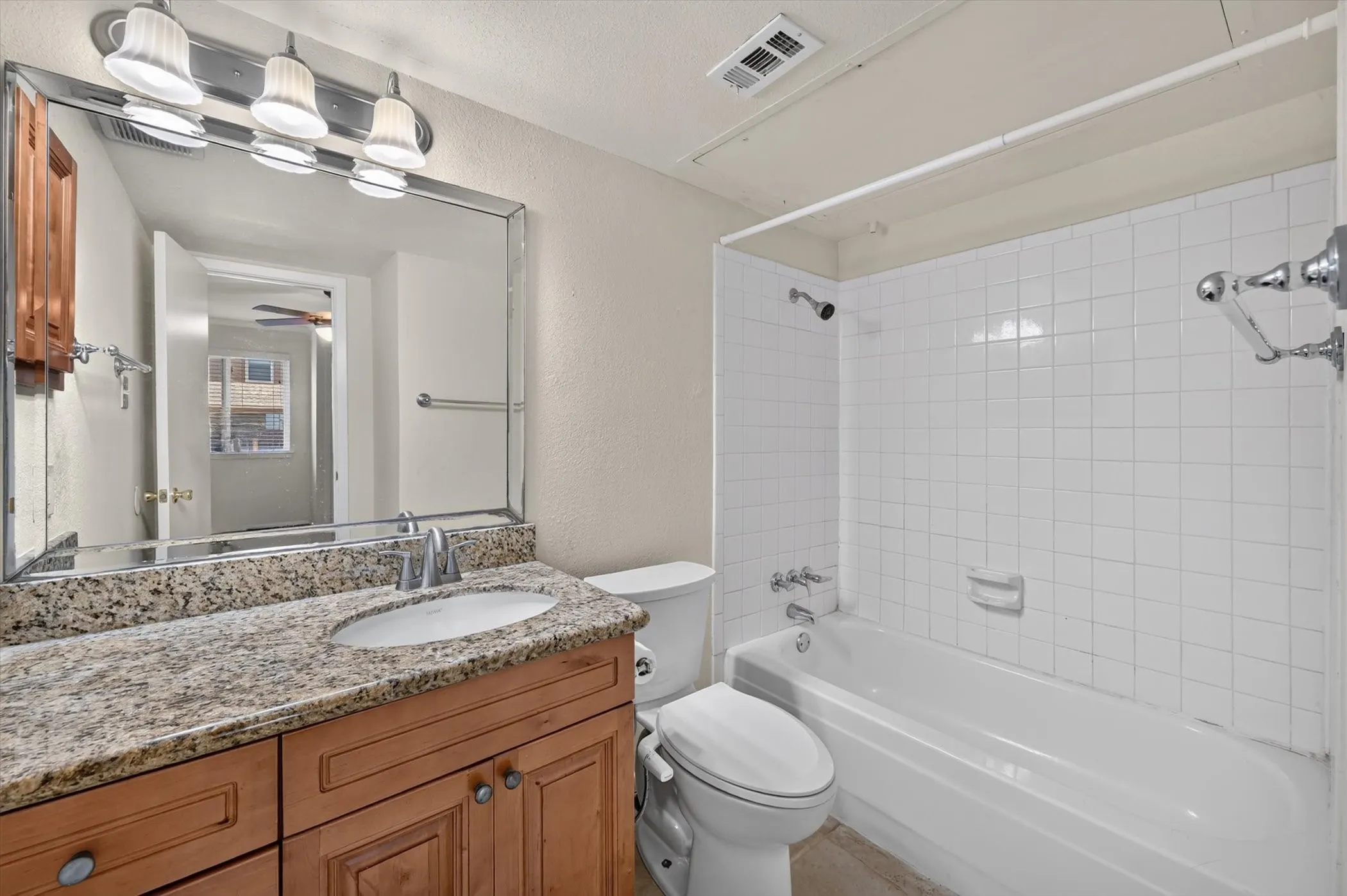 Bathroom featuring a wood-finish vanity with a granite-style countertop and an undermount sink
