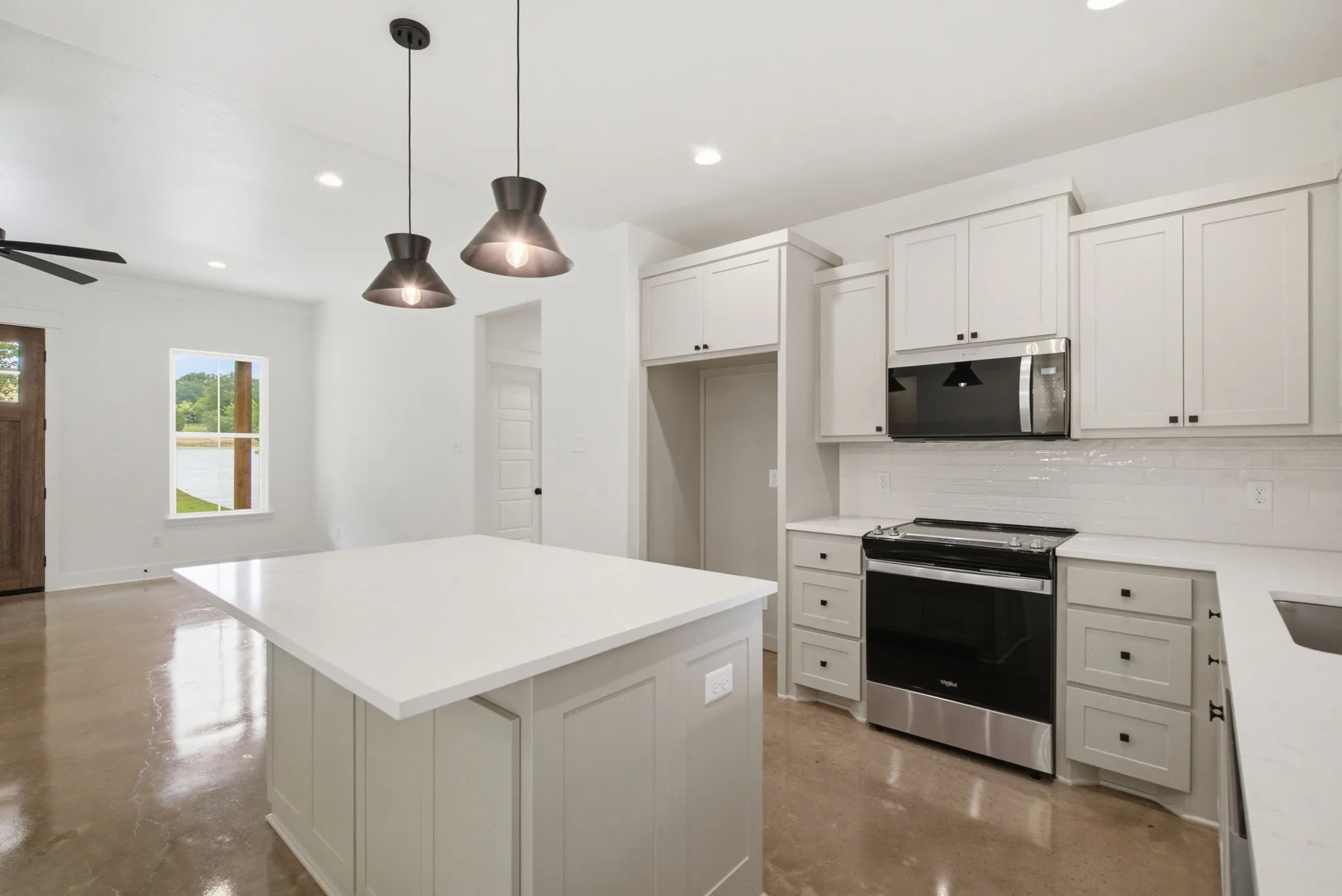 Modern kitchen featuring a large center island with a light-toned countertop, white cabinetry with black hardware, stainless steel and black appliances, and a white subway tile backsplash