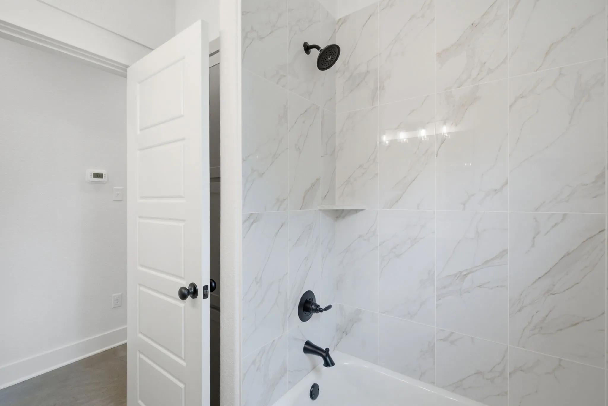 Tub and shower combination featuring large format marble-look tile surround and matte black fixtures
