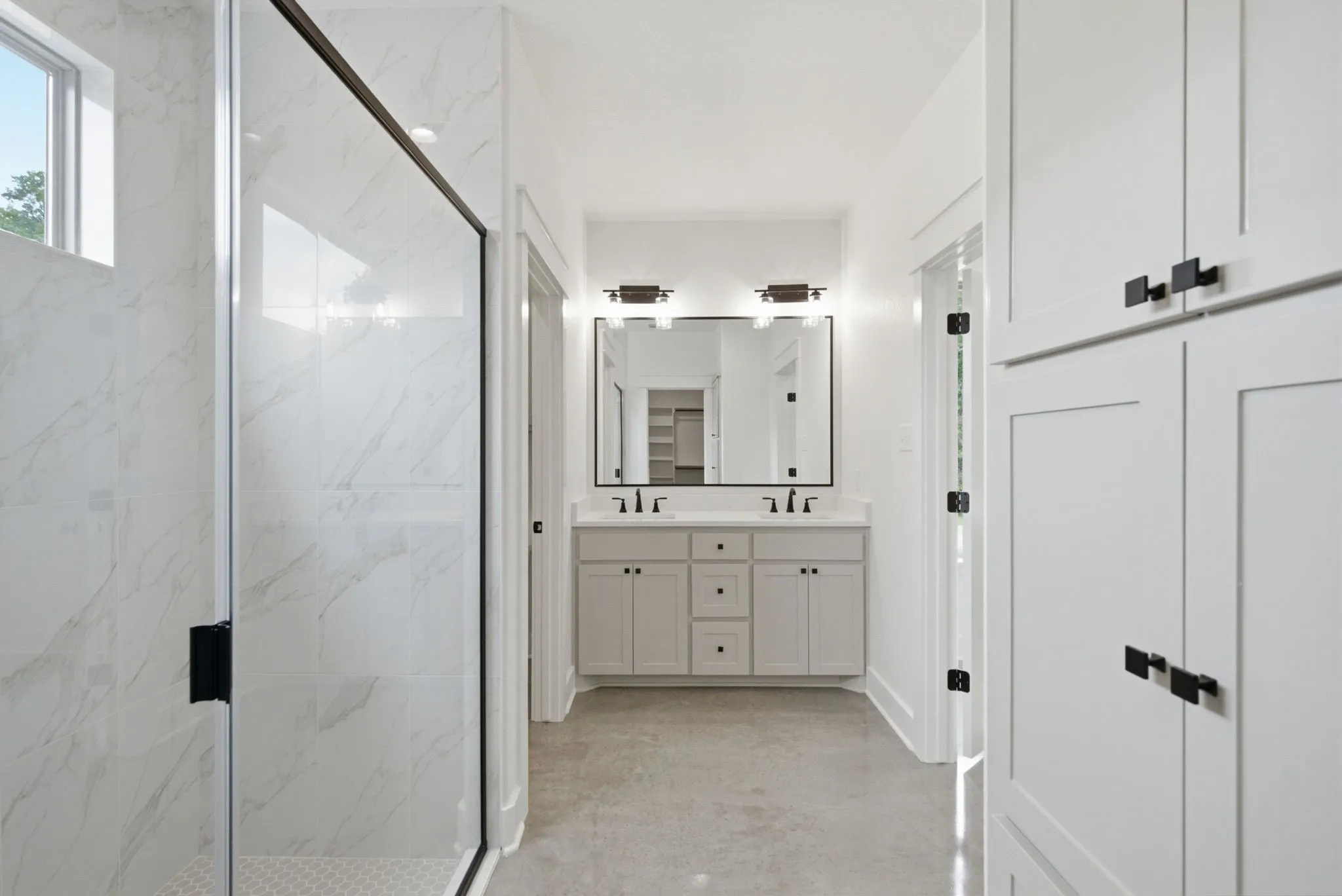 Bright bathroom featuring a double vanity with light gray cabinetry, a frameless mirror, and black hardware
