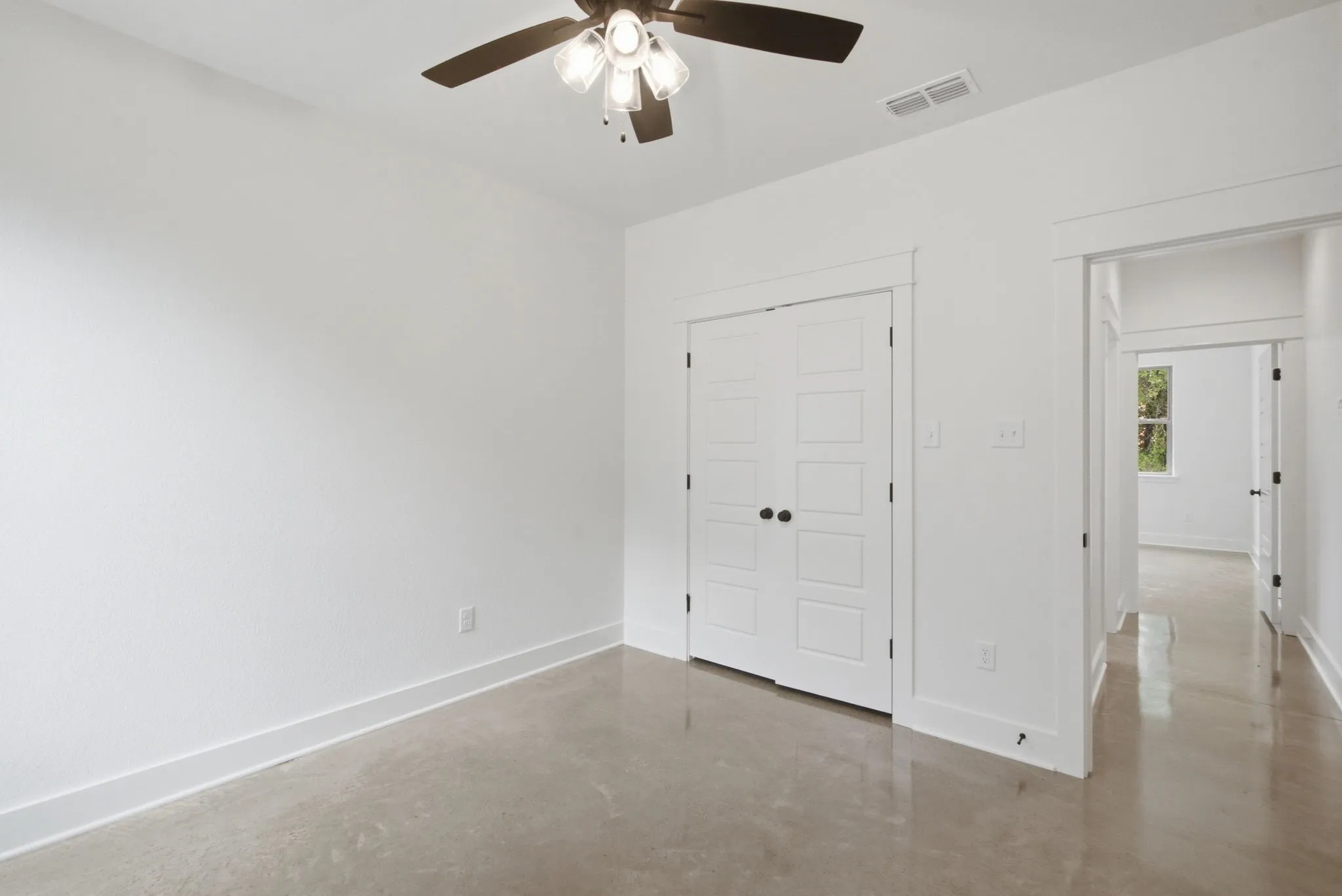 Neutral interior room featuring a ceiling fan with integrated lighting, polished concrete flooring, white walls, and bright white trim