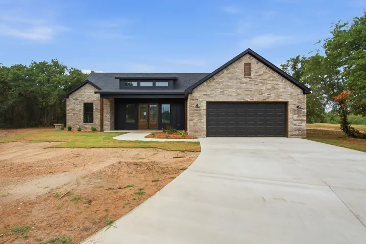 Contemporary home featuring light brick veneer siding, a dark board-and-batten accent, and a black shingle roof