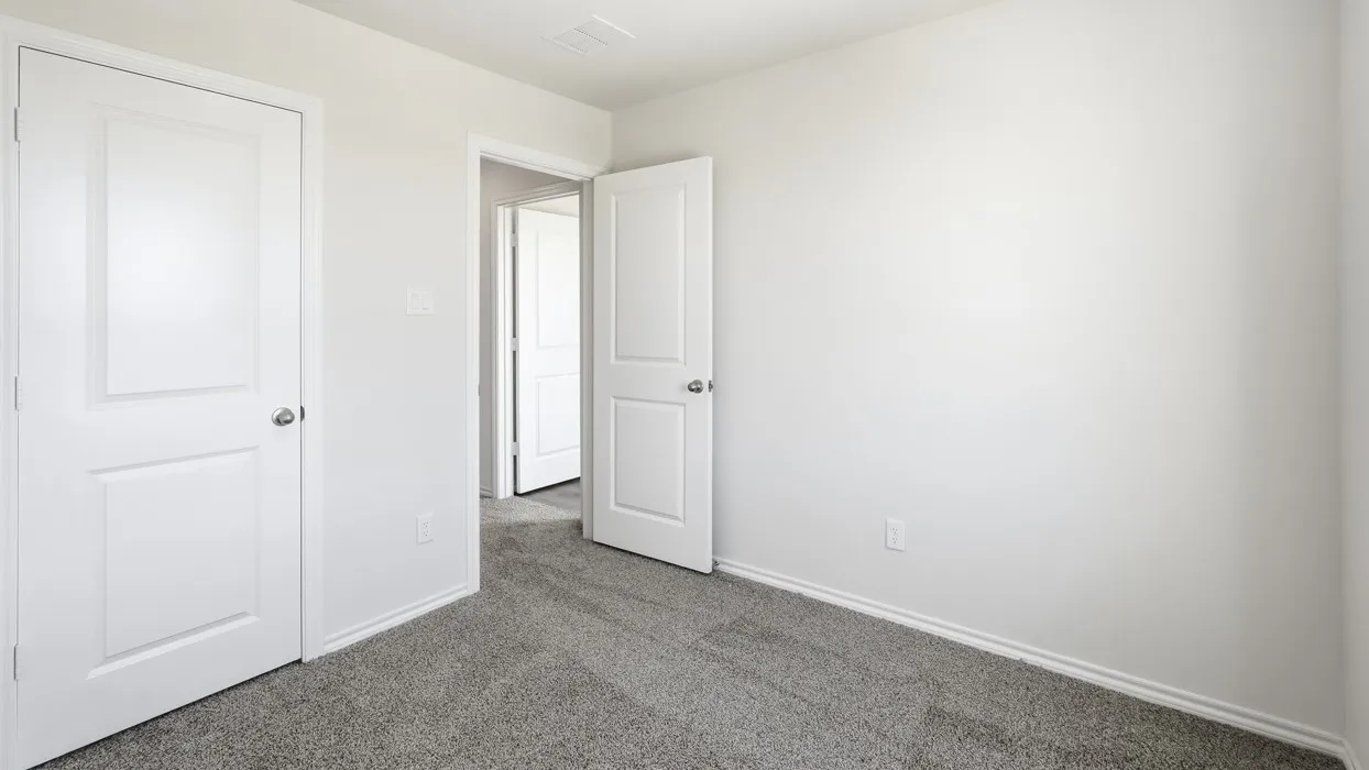 Neutral interior room featuring light grey walls, grey carpet flooring, white baseboards, and white paneled doors with chrome hardware