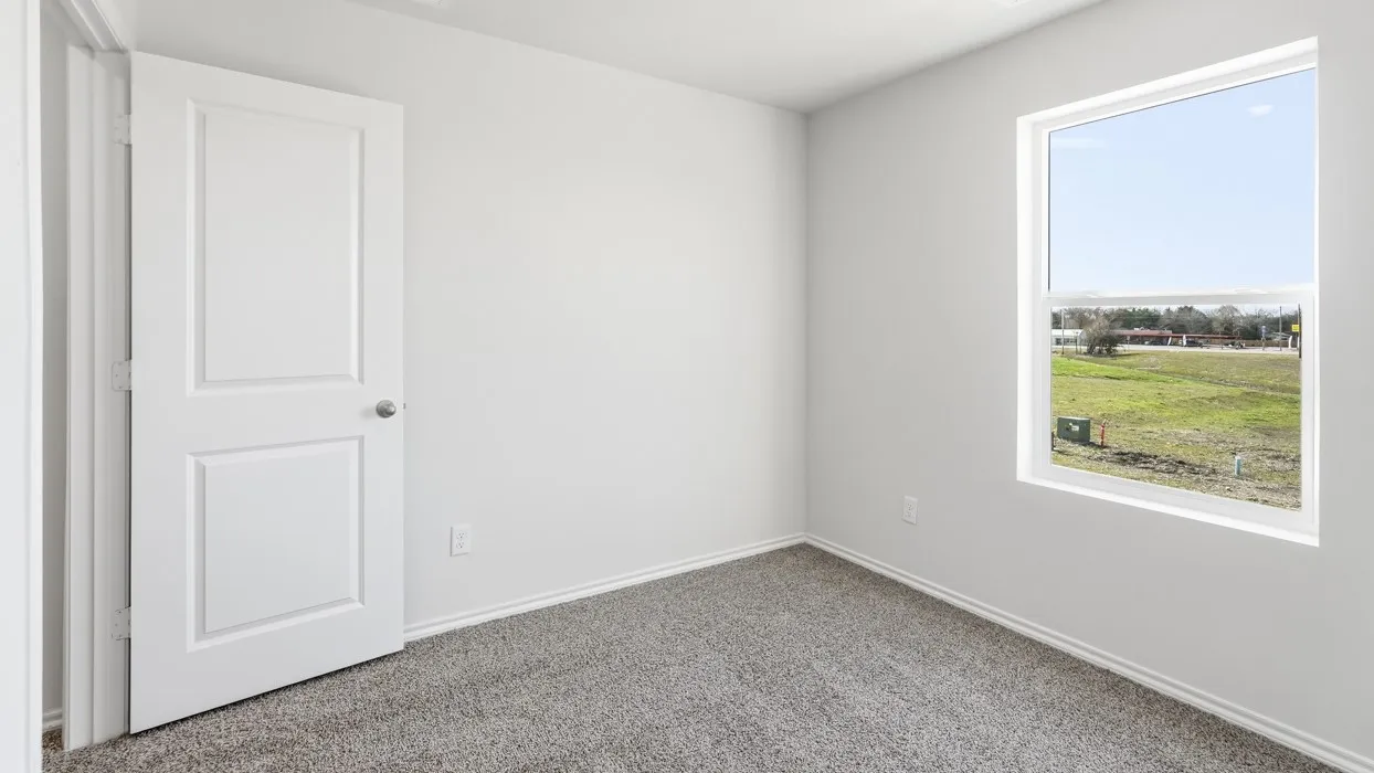 Bright interior room featuring a large window, light gray carpeting, crisp white walls, and a paneled interior door