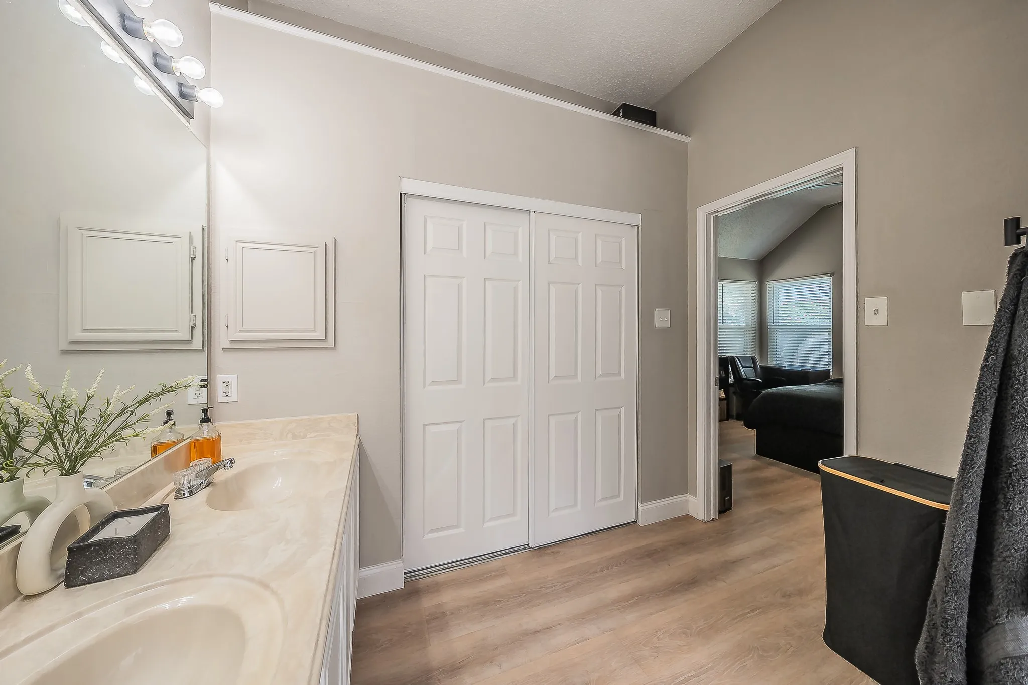 Double vanity with integrated sinks, wood-finish flooring, two-panel bifold closet doors, and light neutral wall tones